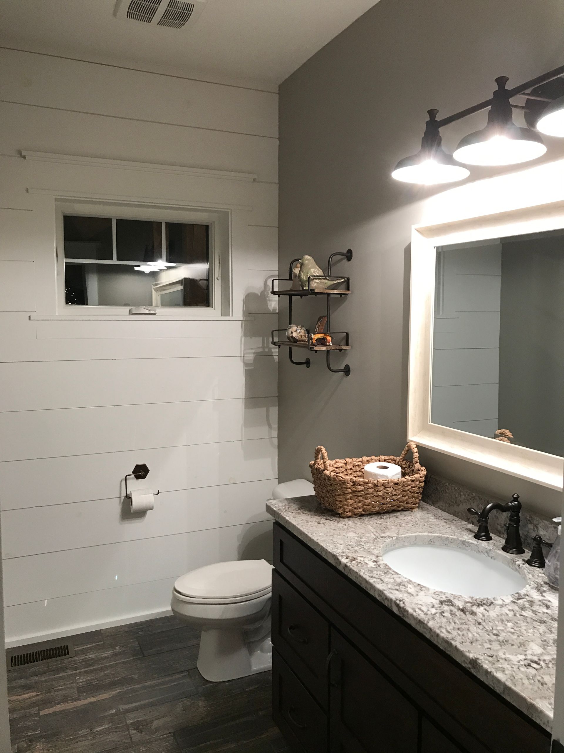 Modern bathroom with granite vanity, sink, toilet, wall mirror, and lighting fixtures