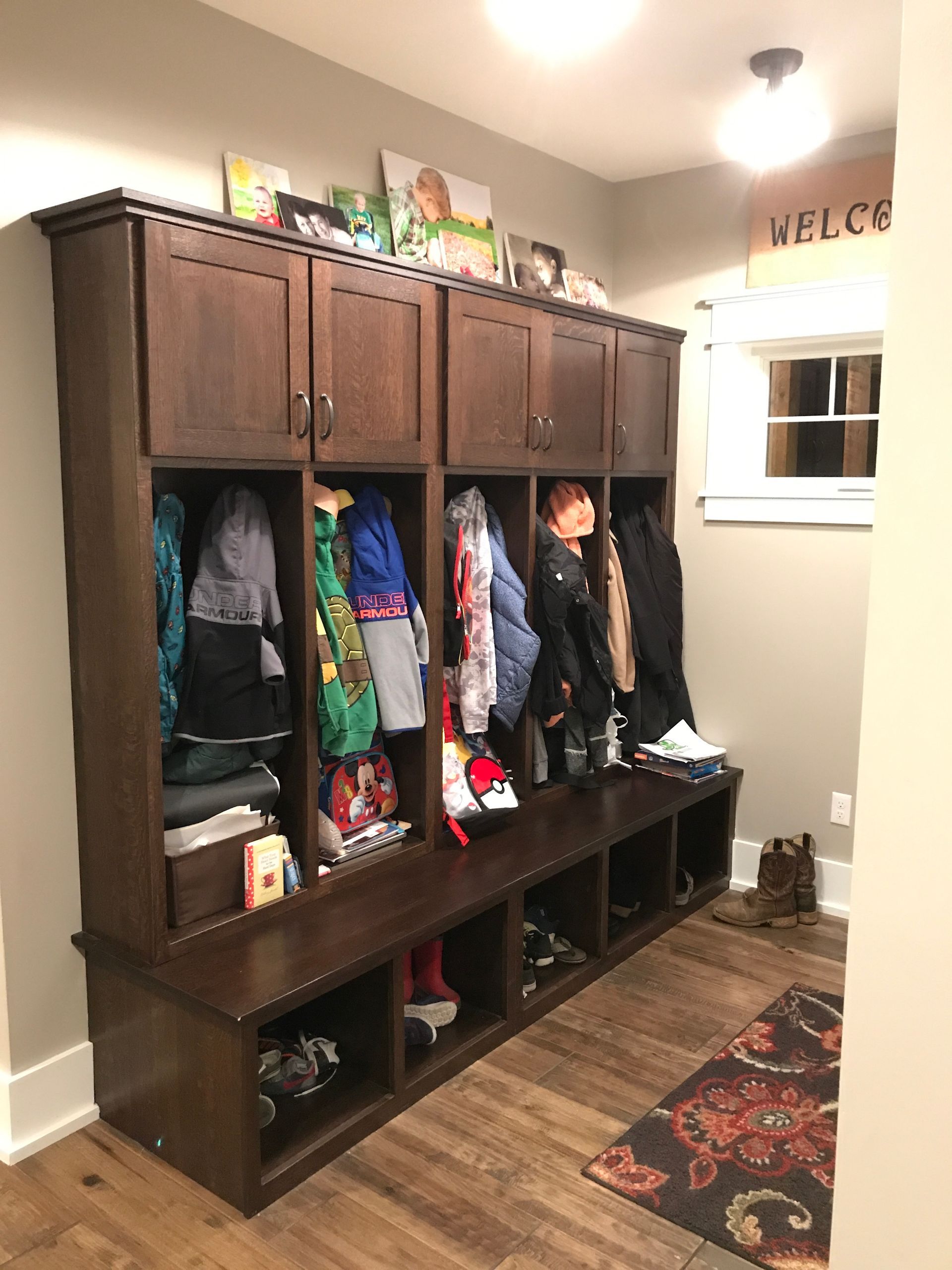 Dark wood cubby coat rack with colorful clothes and shoes in a home entryway.