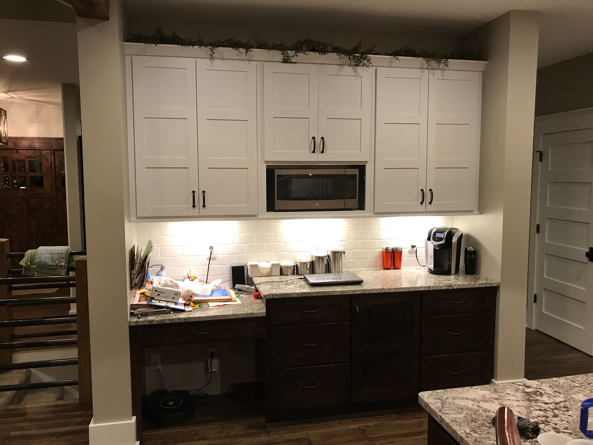Kitchen with white and dark cabinets, lit countertop, microwave, and coffee maker under an arched alcove.