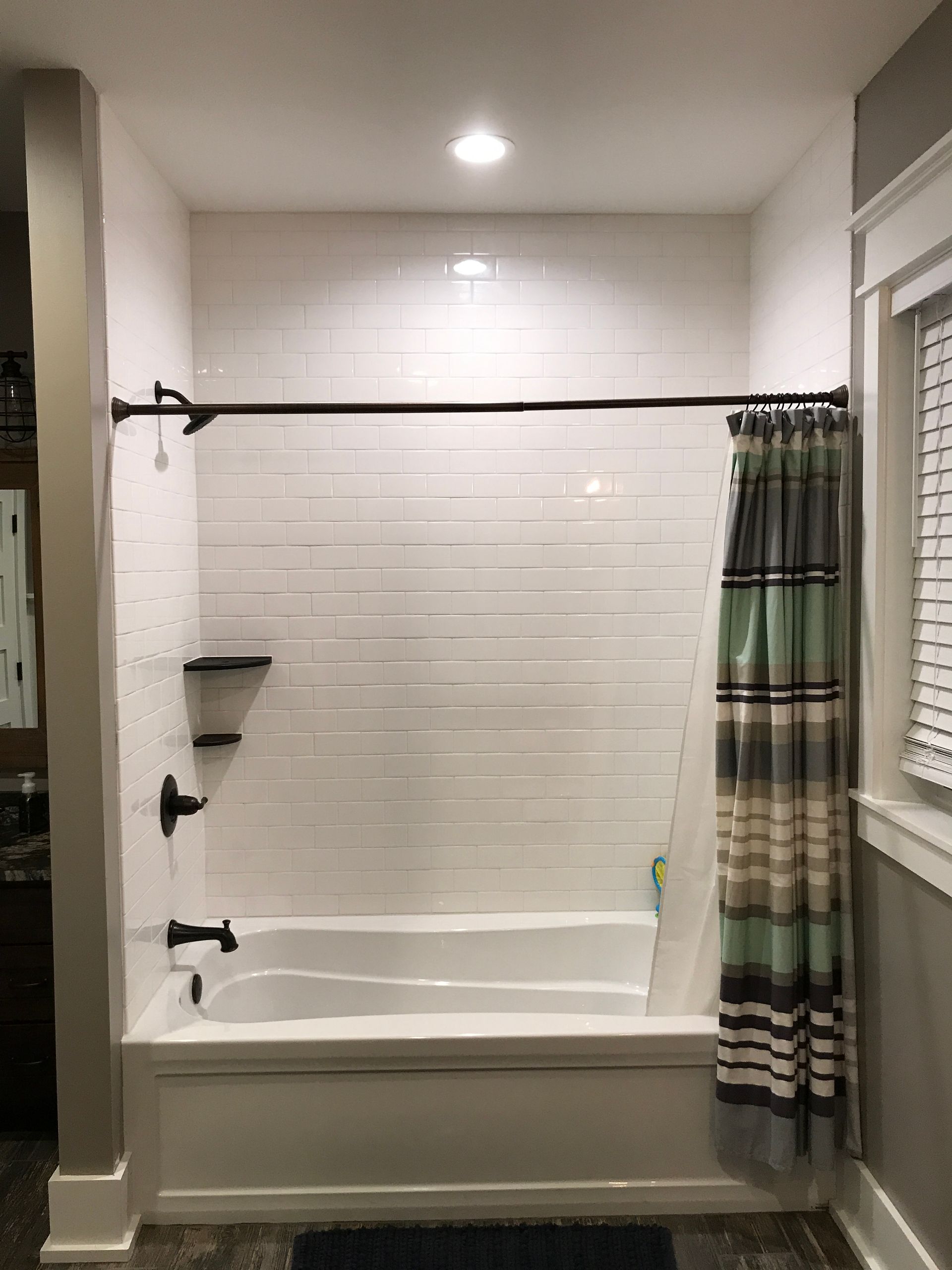 Bathroom with a white tiled tub-shower, black shower rod, and striped curtain partially drawn aside