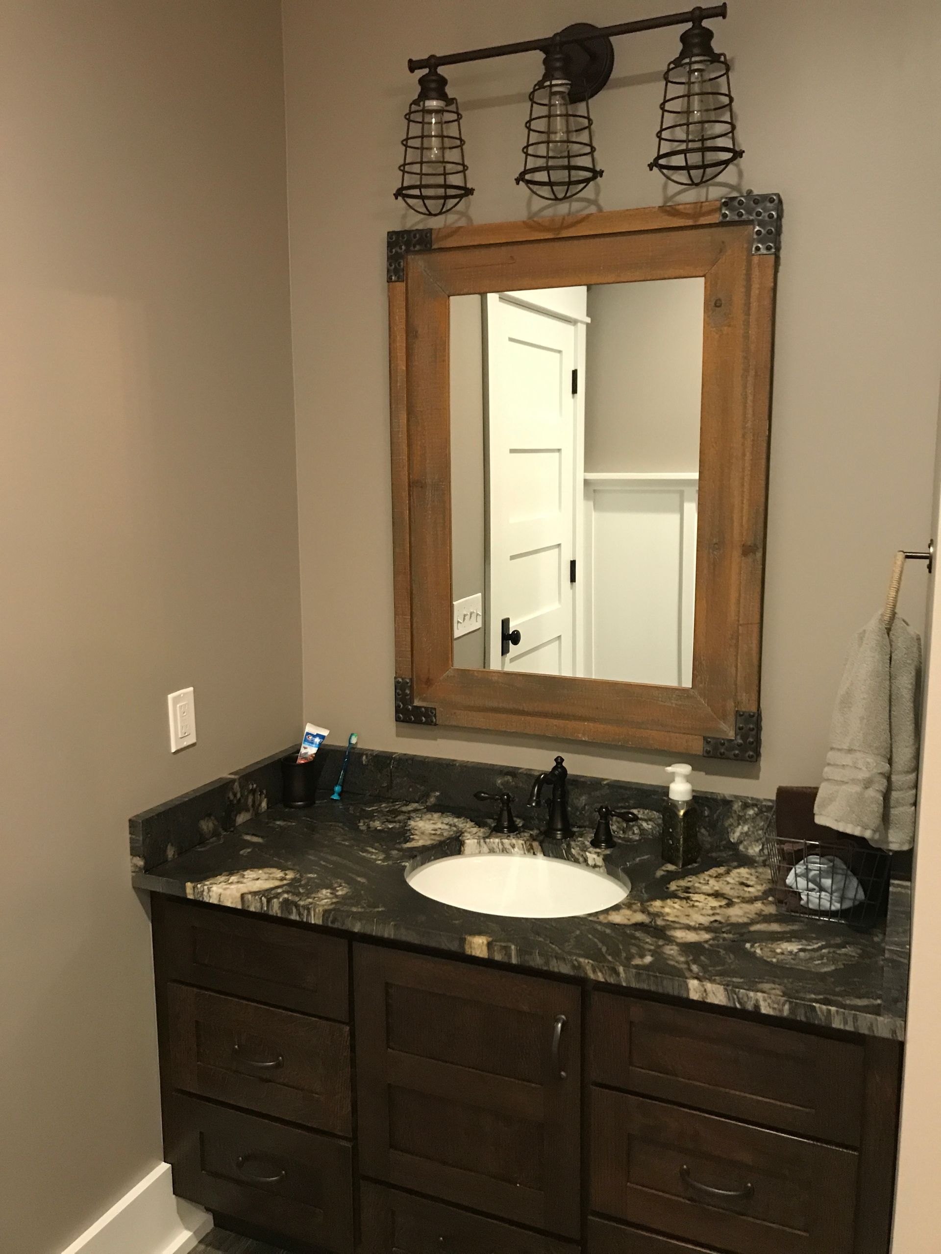 Bathroom vanity with granite countertop, round sink, wood-framed mirror, and three pendant lights above.