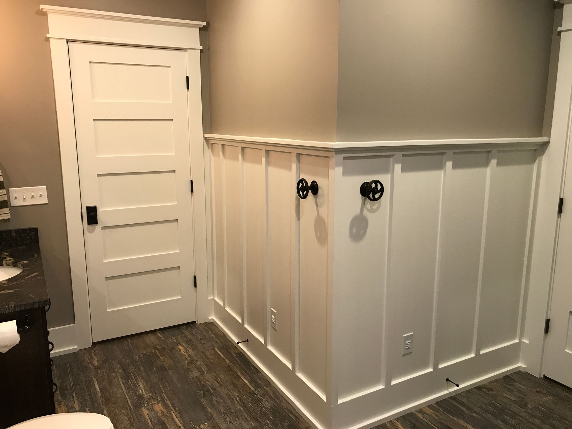 White paneled hallway with a closed door, dark wood floor, and gray walls with white wainscoting