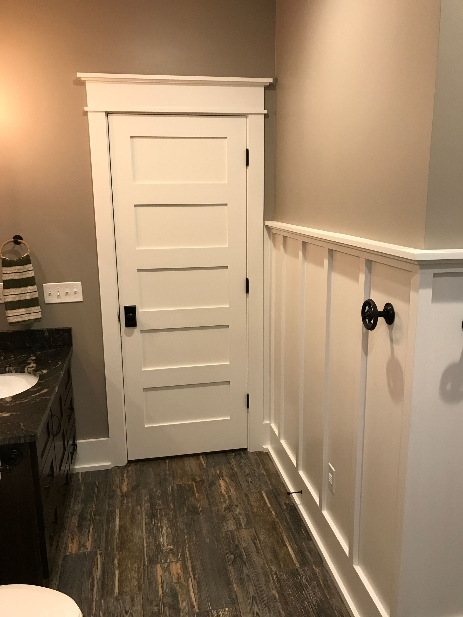 Narrow hallway with a white paneled door, gray walls, dark wood floor, and a partial bathroom vanity on the left