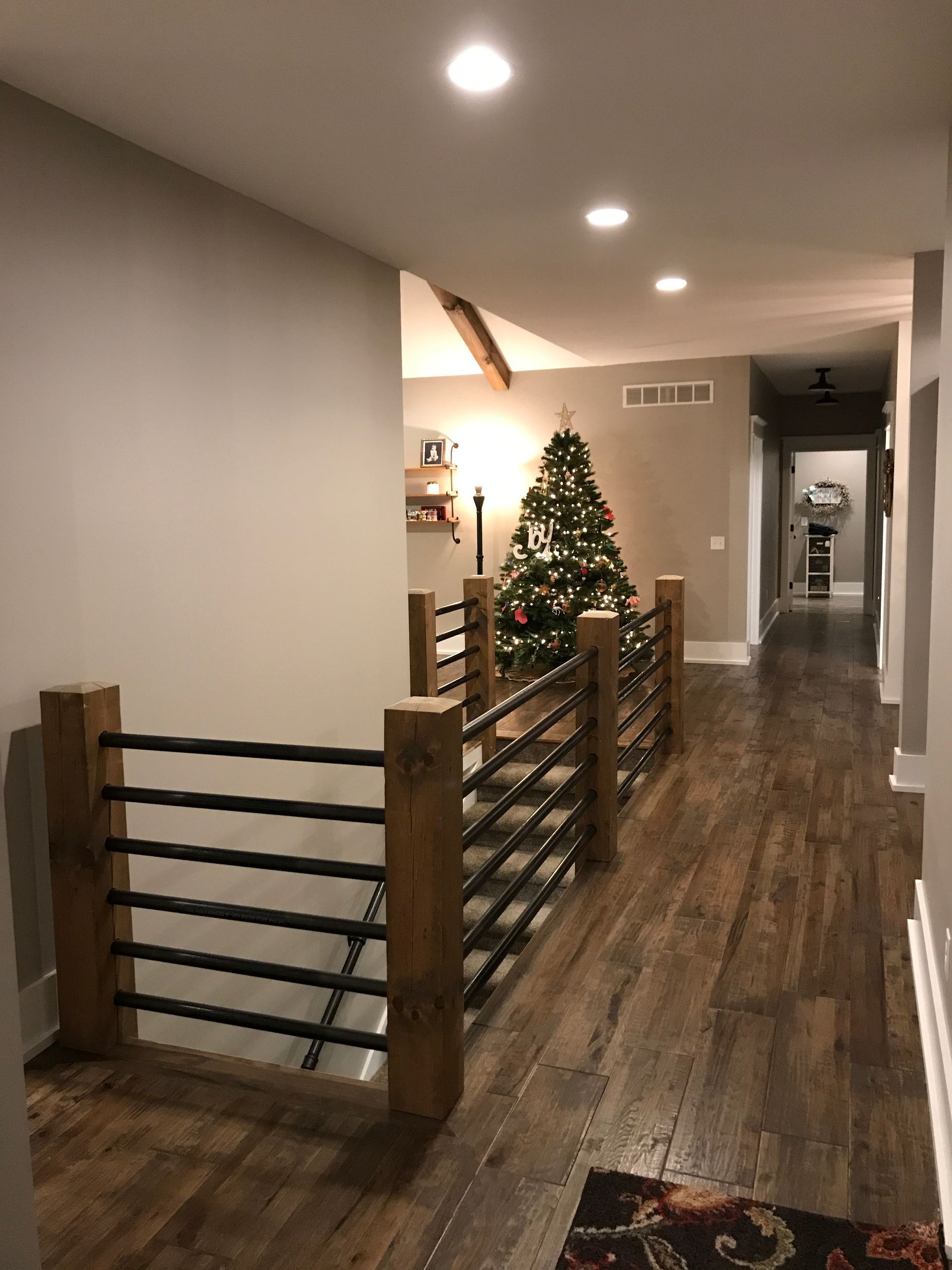 Hallway with wood floors, black railing, and a lit Christmas tree near the wall