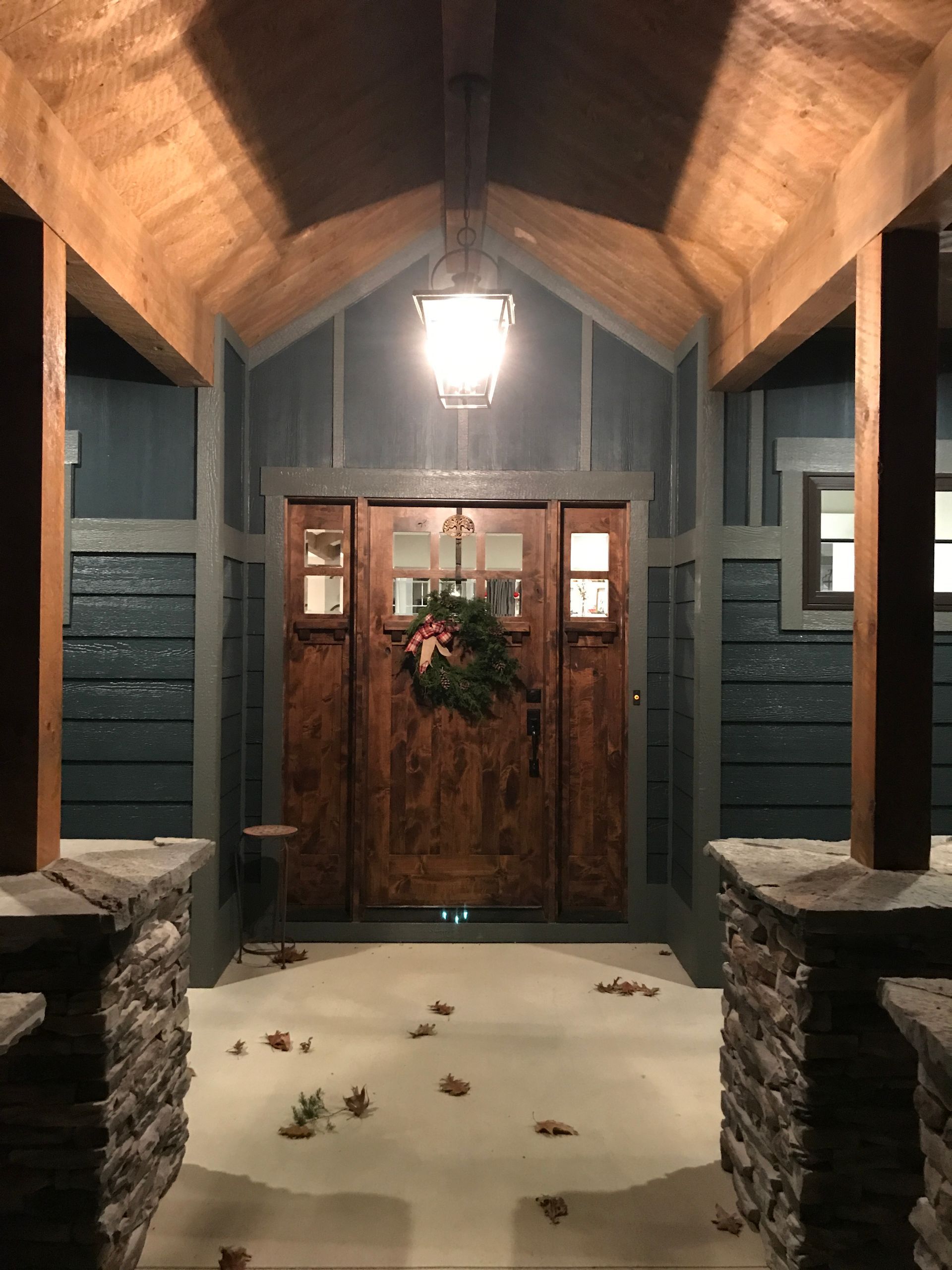 Covered front porch with stone pillars, wood ceiling, and double wooden doors decorated with a wreath.