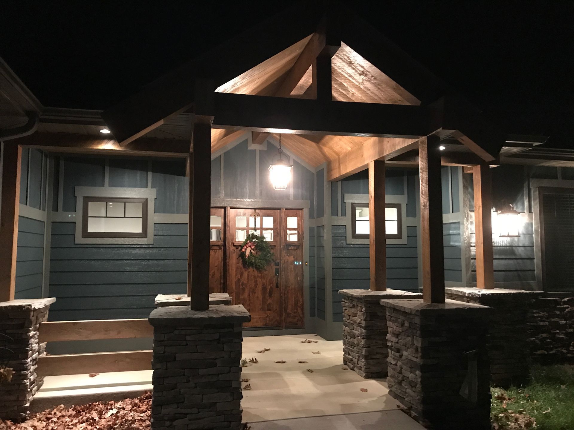 Lit house entrance with stone pillars and wooden double doors at night