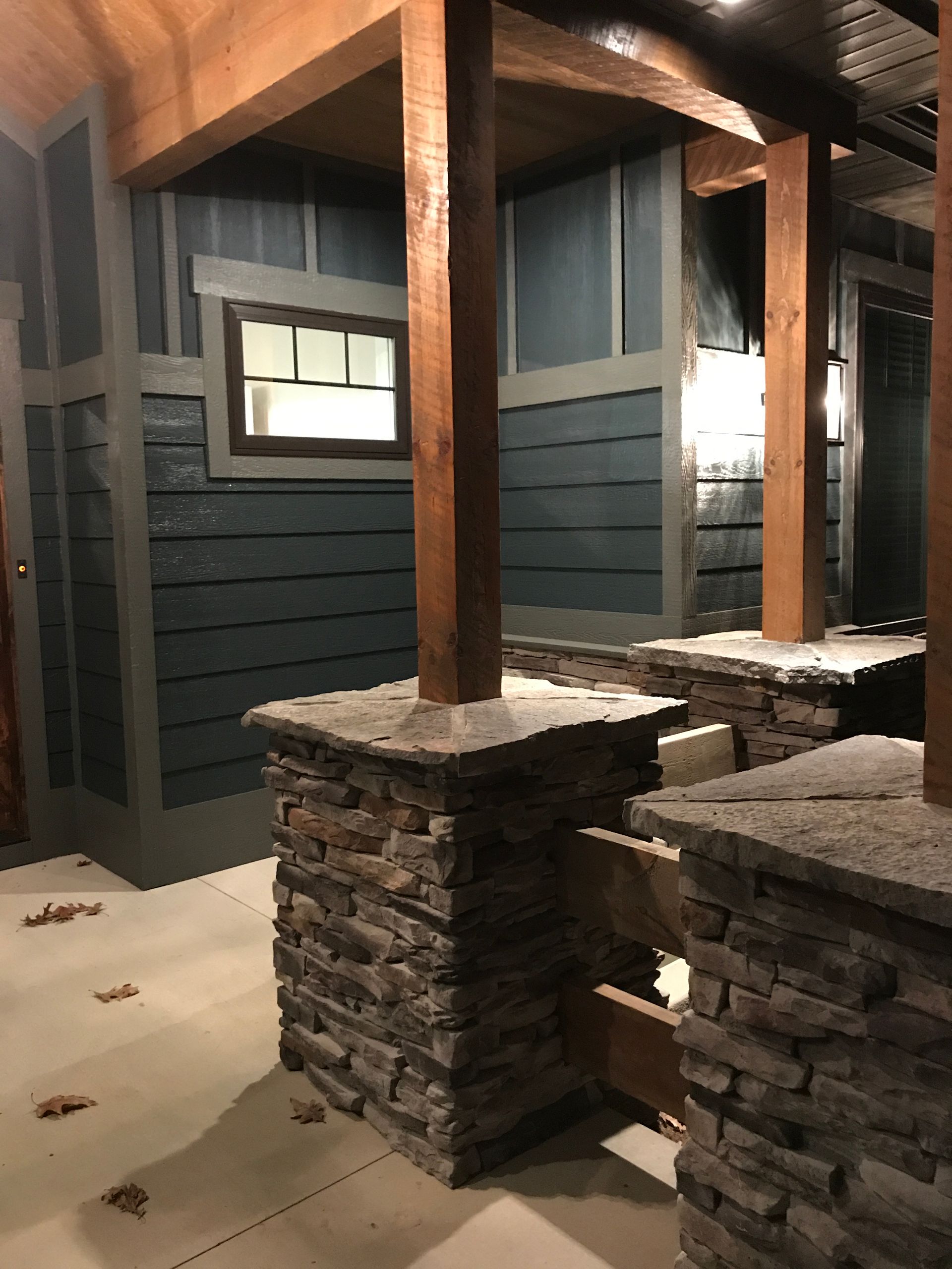 Covered porch with stone pillars, wood beams, and dark siding at night