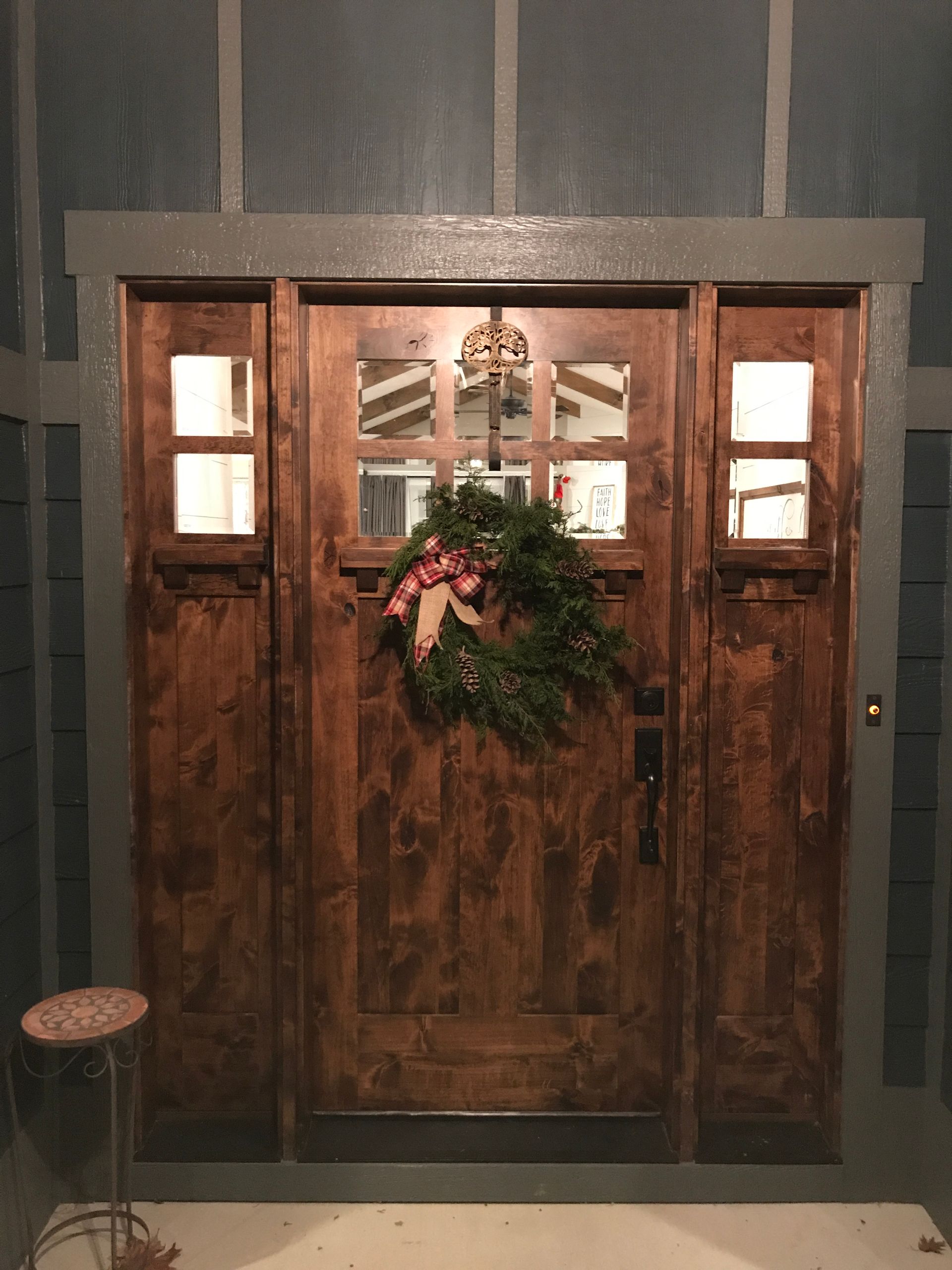 Rustic wooden double doors with glass panes and a holiday wreath, framed by dark gray walls.