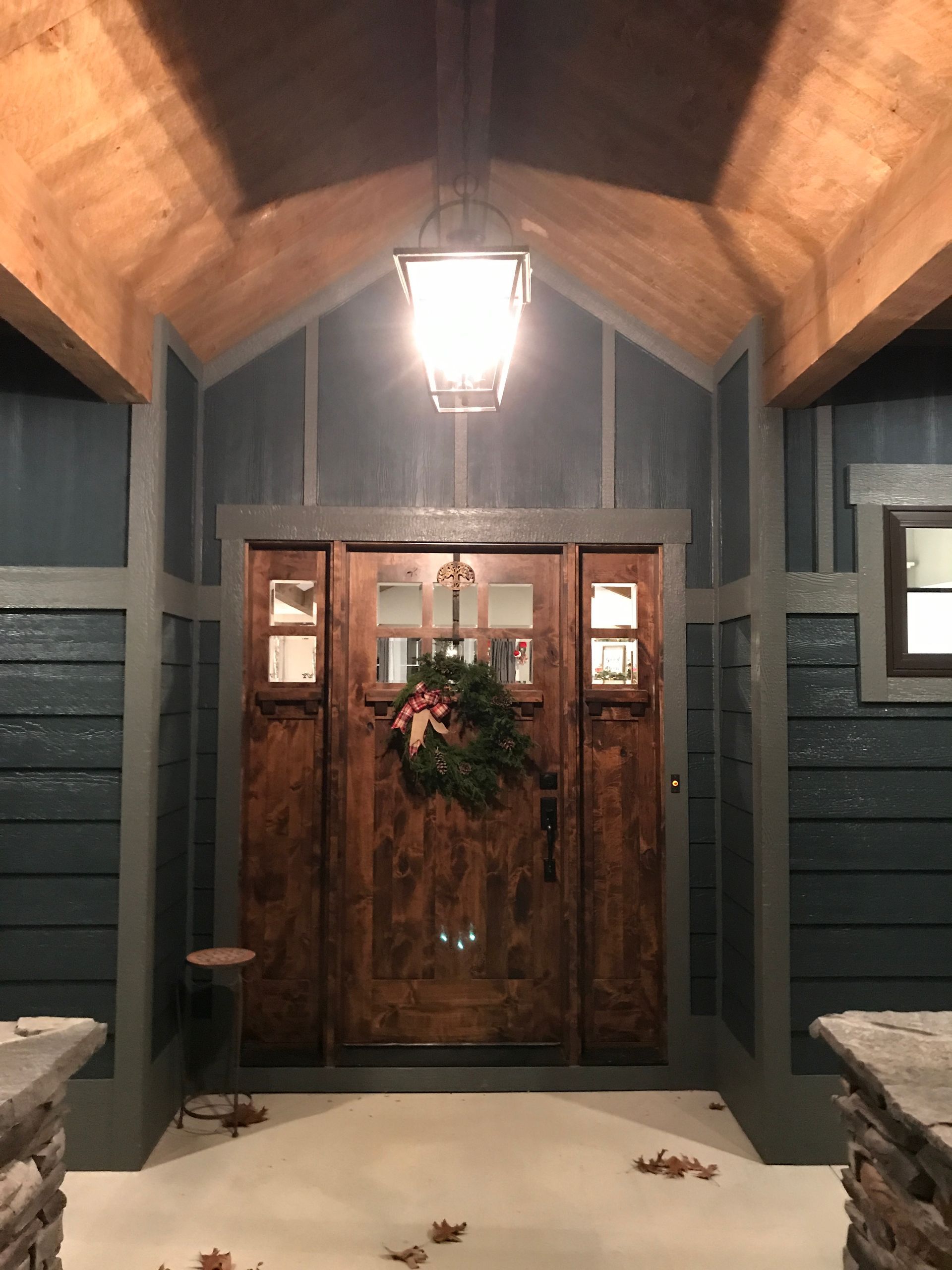 Front porch with wooden double doors, a hanging lantern, teal siding, and a holiday wreath with snow on the steps