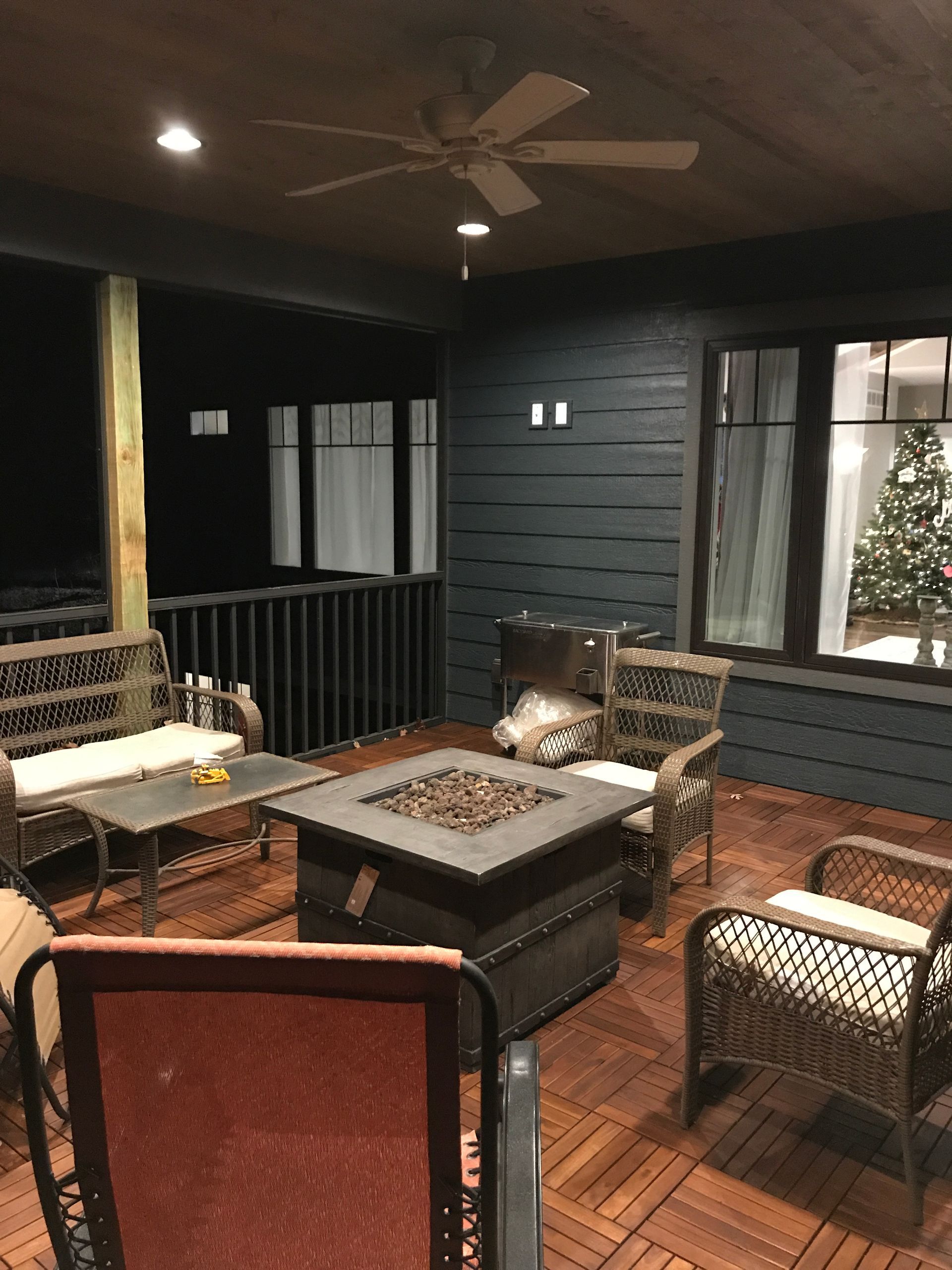 Covered patio with wicker seating, fire pit table, and ceiling fan at dusk.
