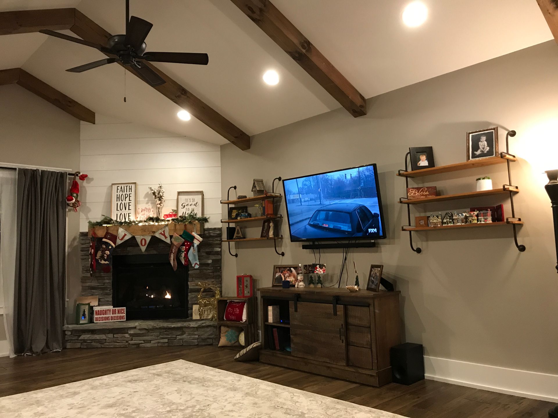 Living room with vaulted ceiling, mounted TV, fireplace, wooden shelves, and rustic decor