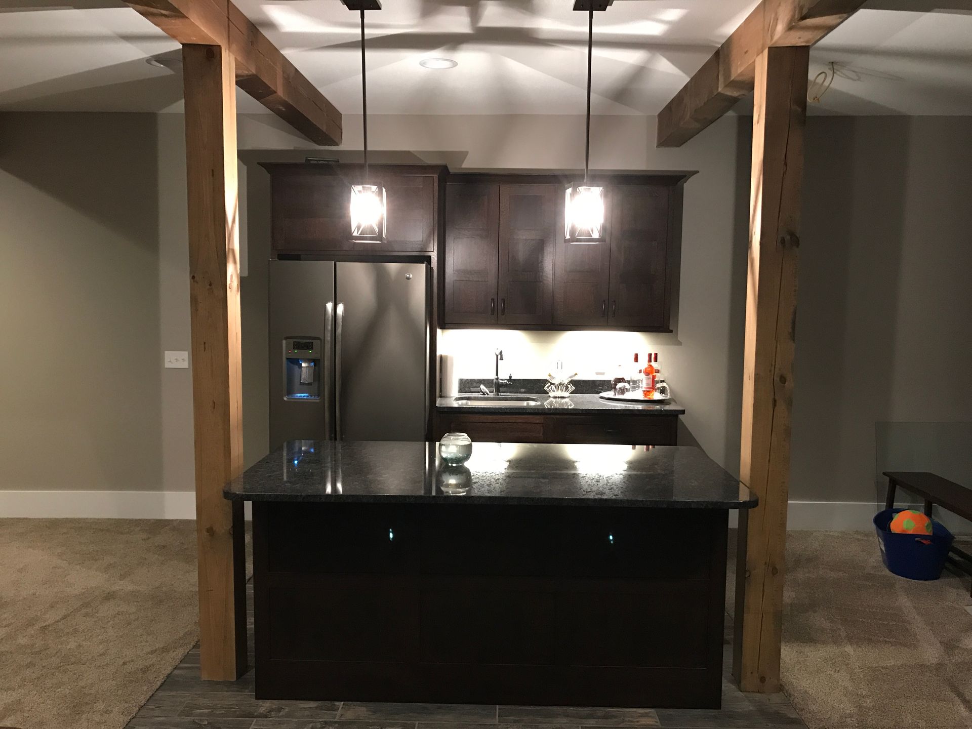 Basement kitchen with dark cabinets, black island, and exposed wooden beams