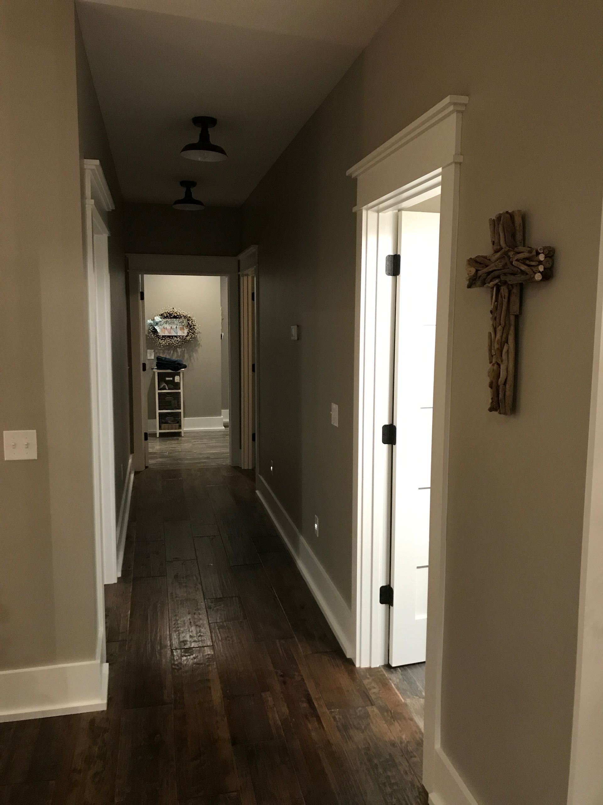 Long hallway with dark wood floors, gray walls, white trim, and a crucifix on the right wall.
