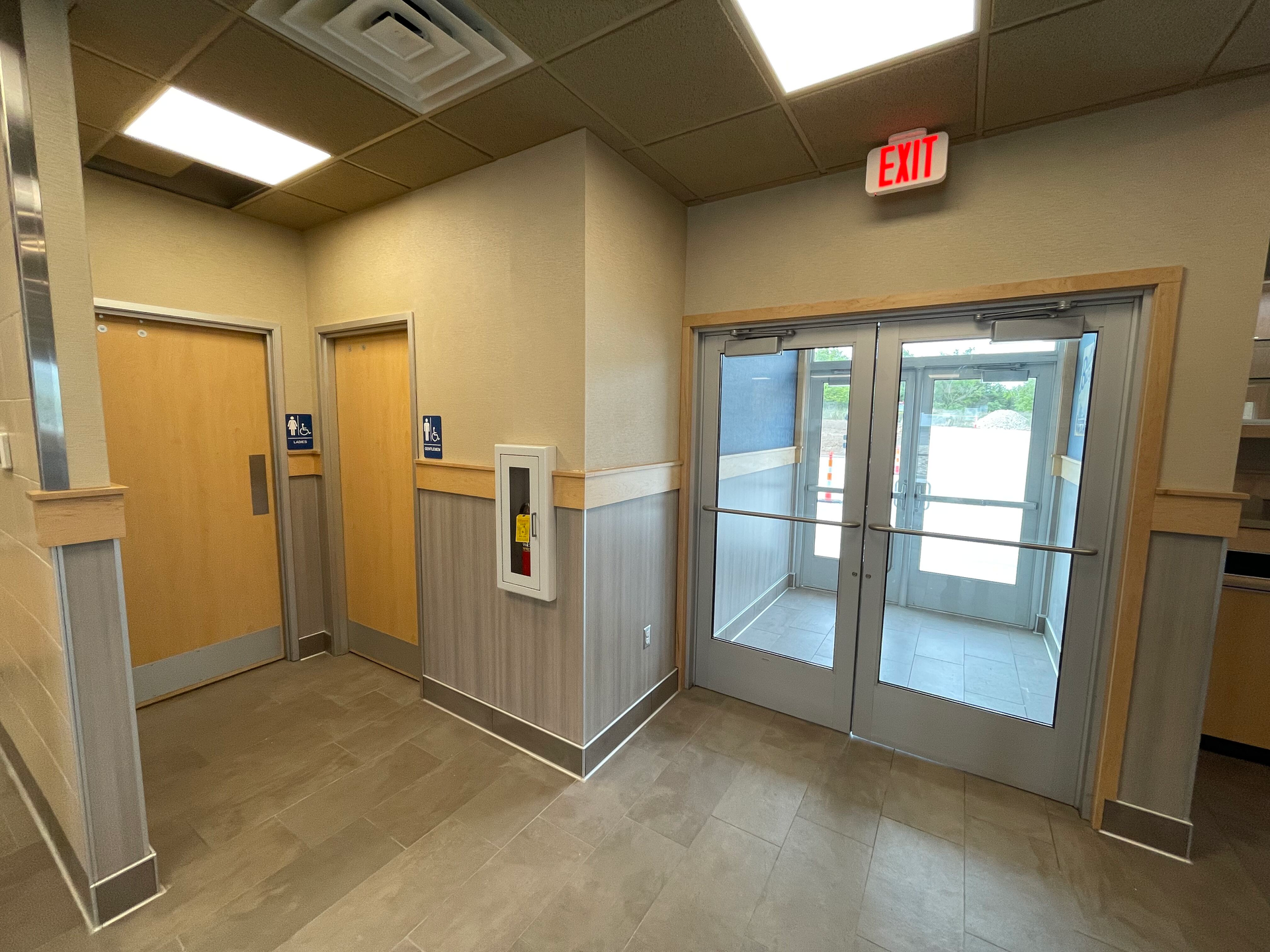 Office lobby with glass exit doors, wood-paneled walls, and an illuminated exit sign.