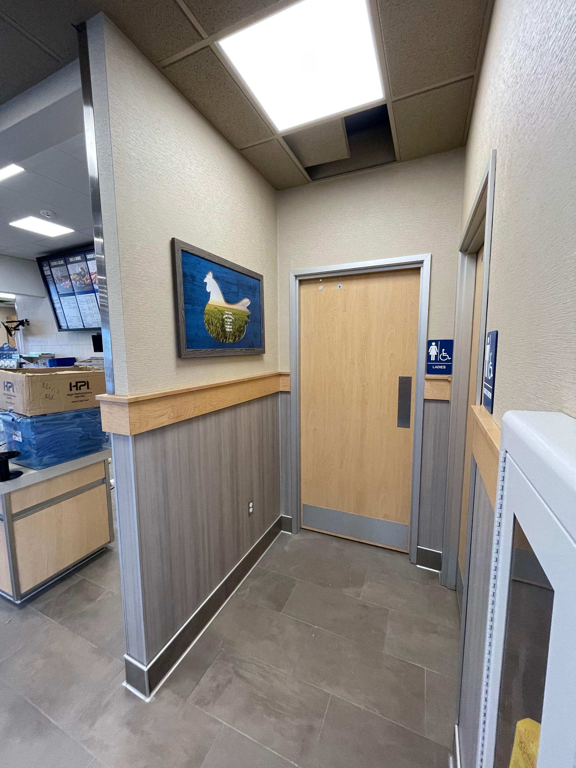 Narrow hallway with beige door, blue wall art, wood trim, and tile floor in an office or public building