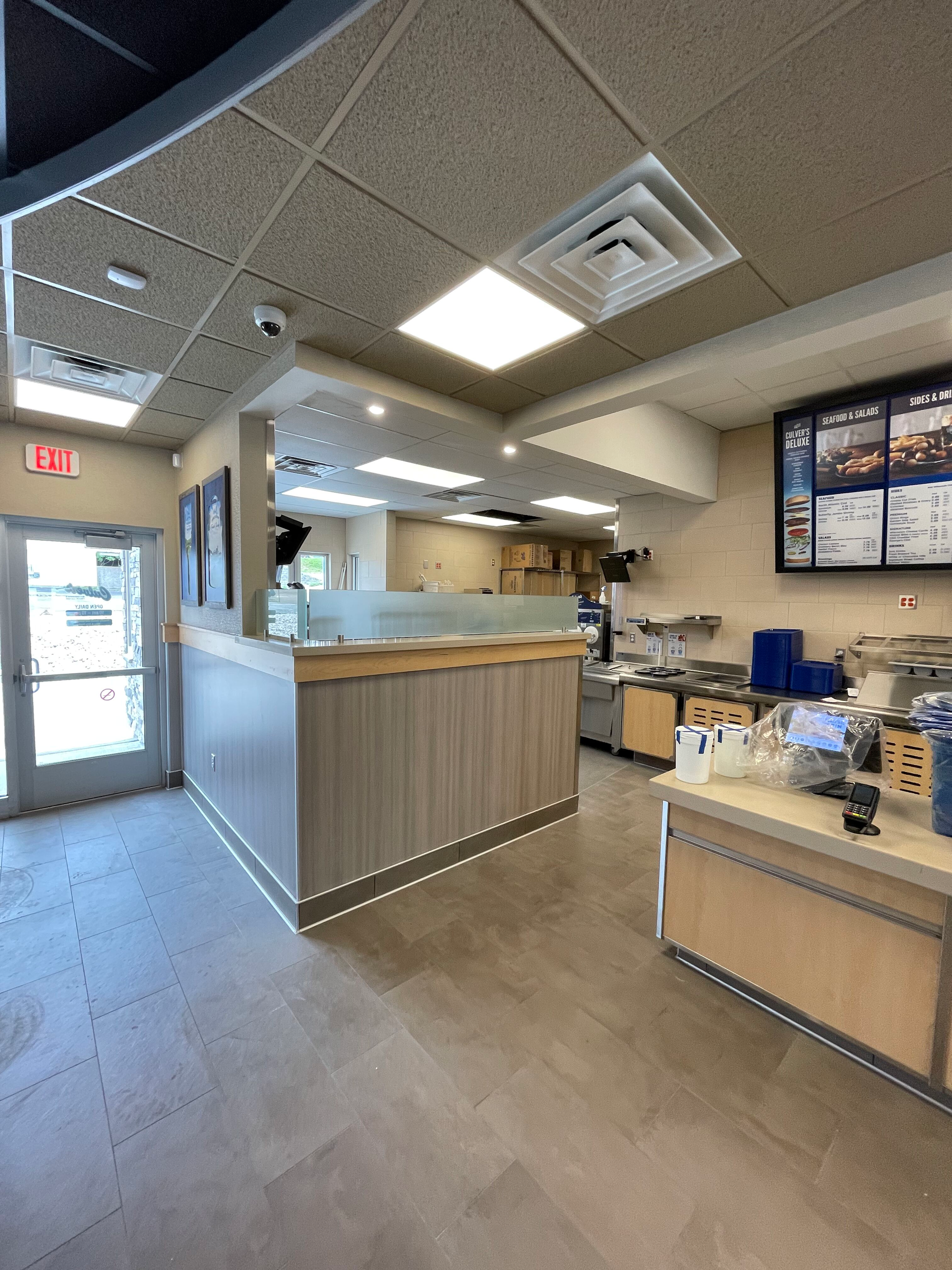 Empty fast-food counter with menu boards, blue chairs, and a doorway in a bright indoor dining area