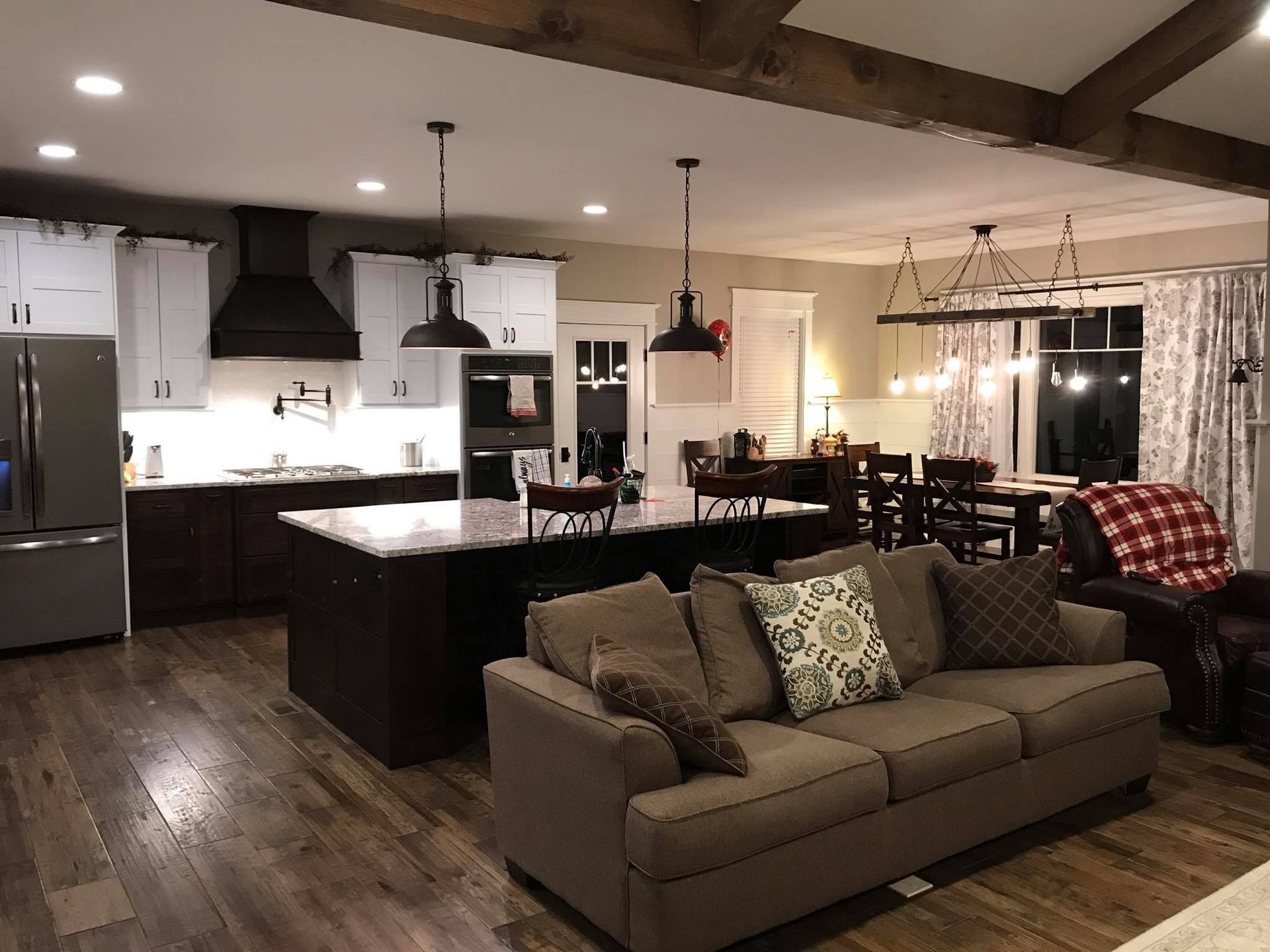 Open-plan living room and kitchen with brown sofa, dark wood floors, white cabinets, and pendant lights