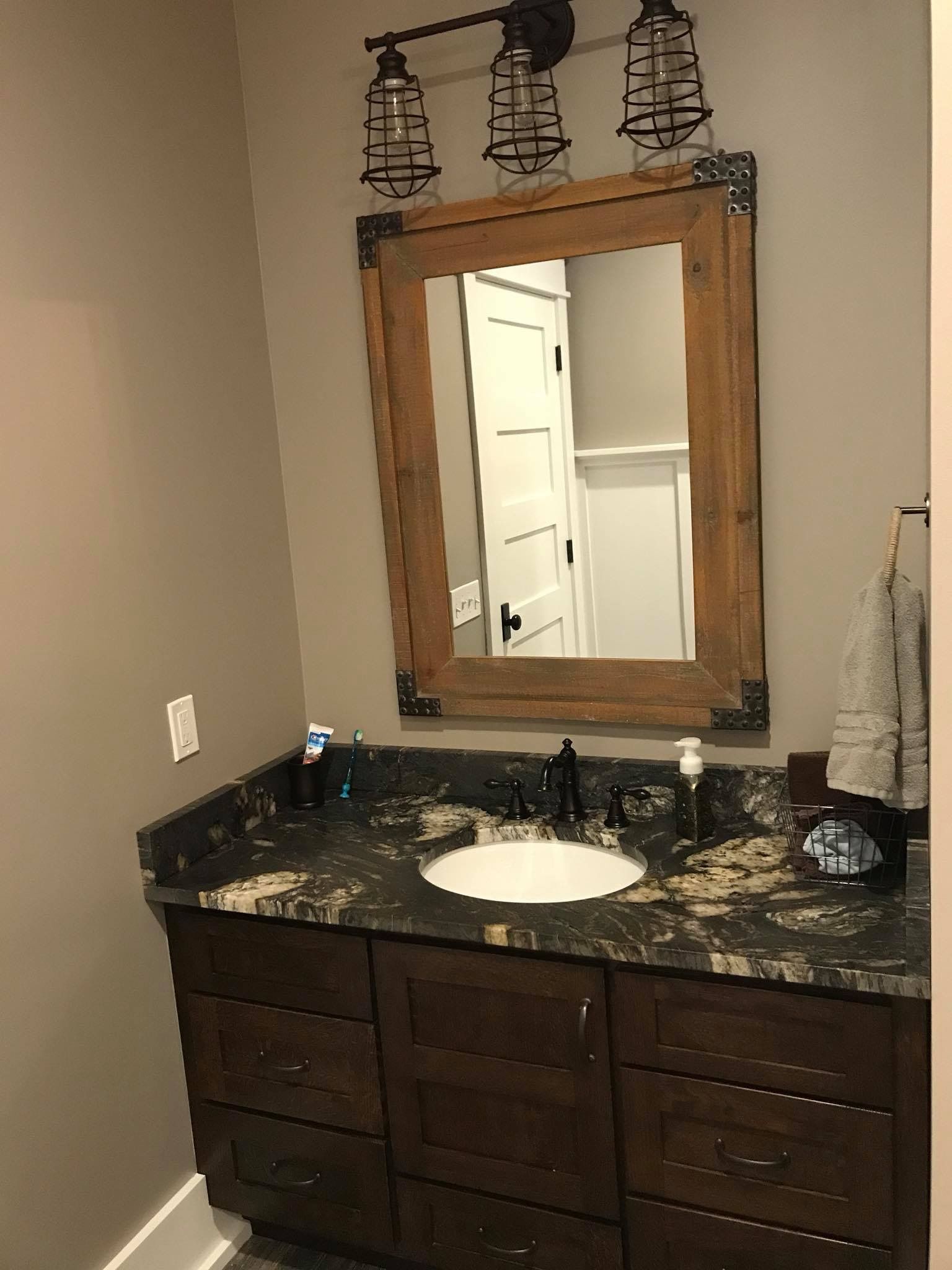 Bathroom vanity with dark granite countertop, wood-framed mirror, and black wall lights.