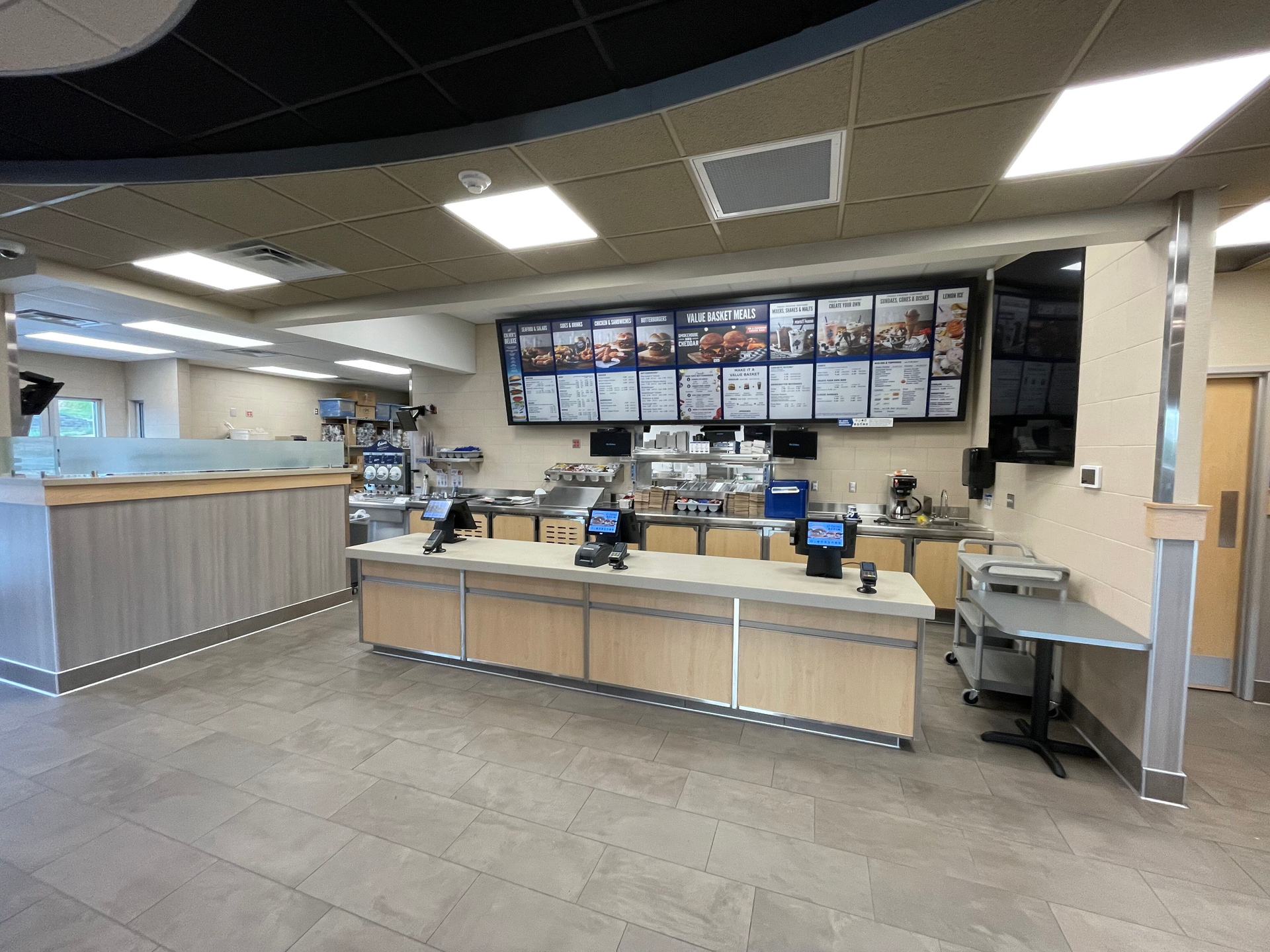 Fast-food restaurant counter with menu boards, cash registers, and empty seating area