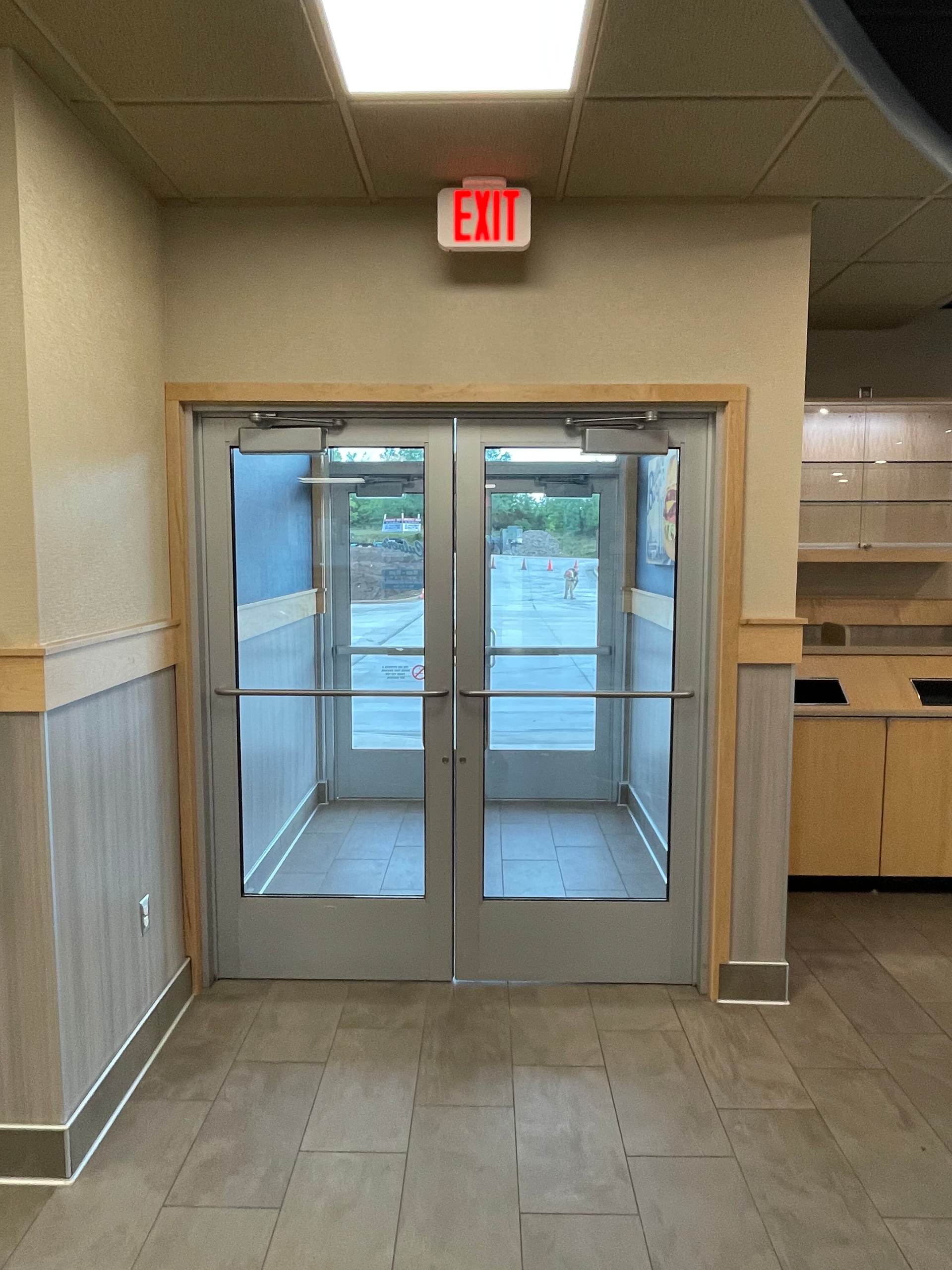 Interior hallway with double glass exit doors and a red EXIT sign above them.
