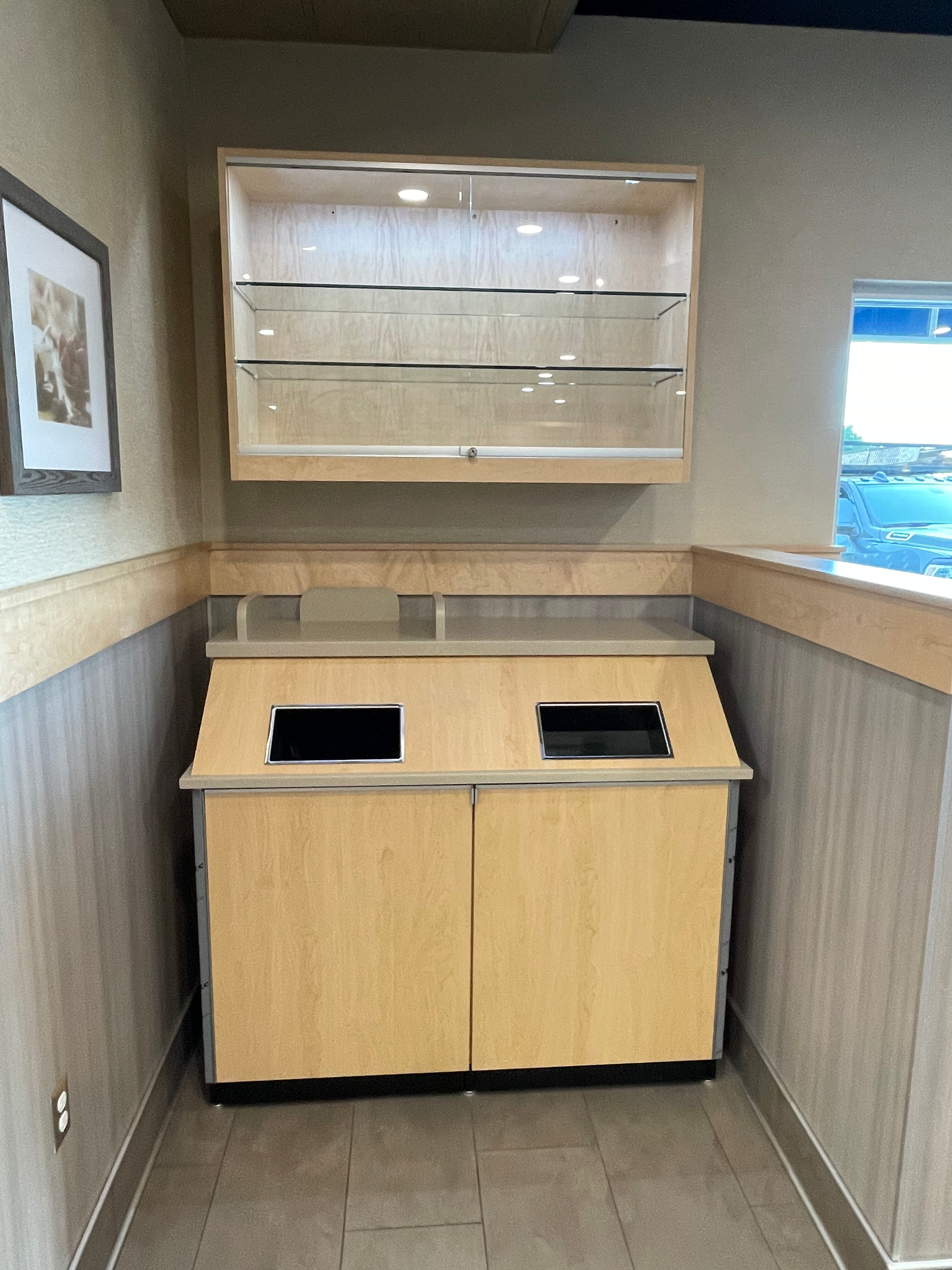 Small room with a wood counter and two black openings beneath wall shelves and a window.