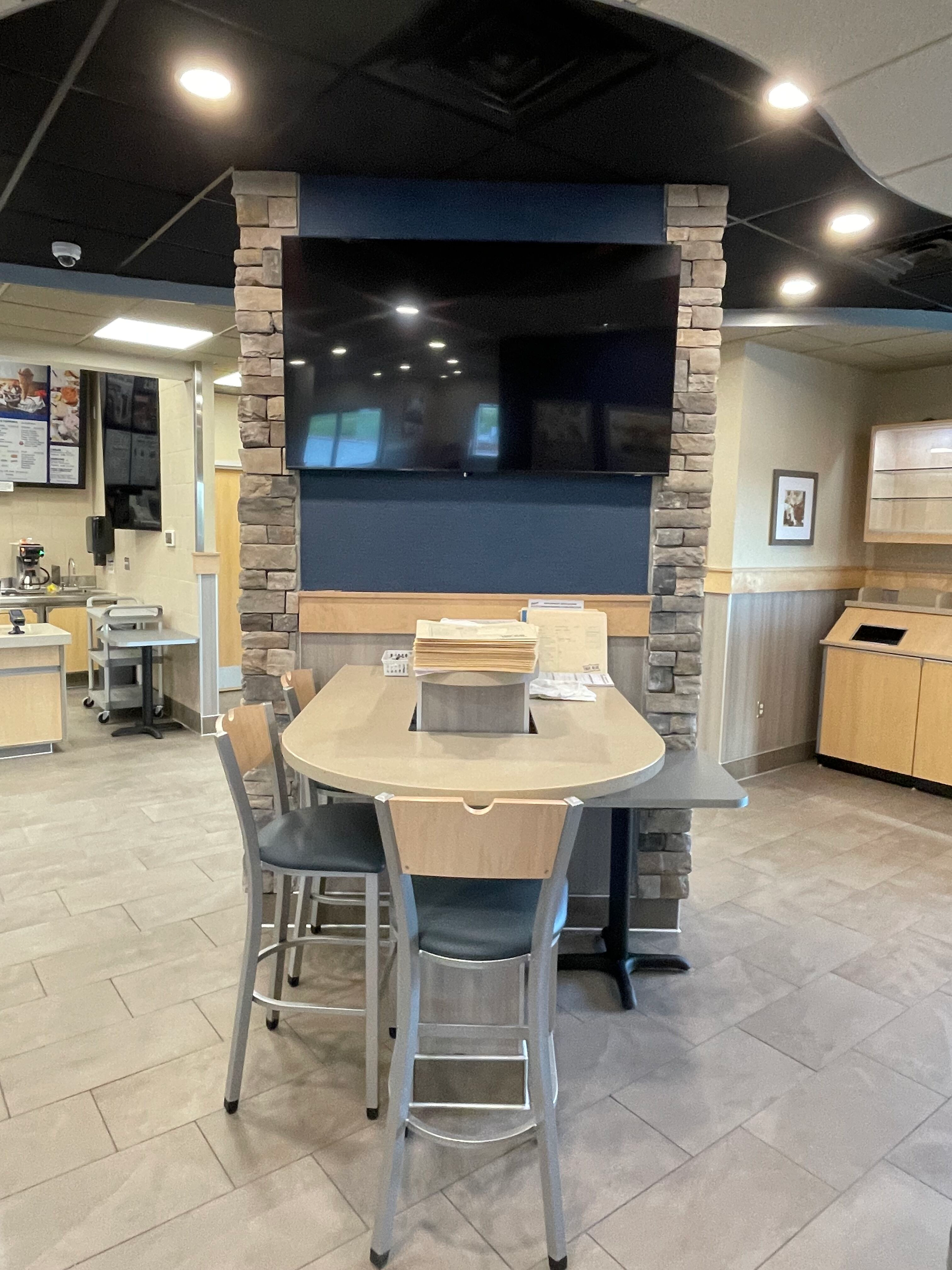 Restaurant dining area with a large wall-mounted TV and a table with chairs in the foreground