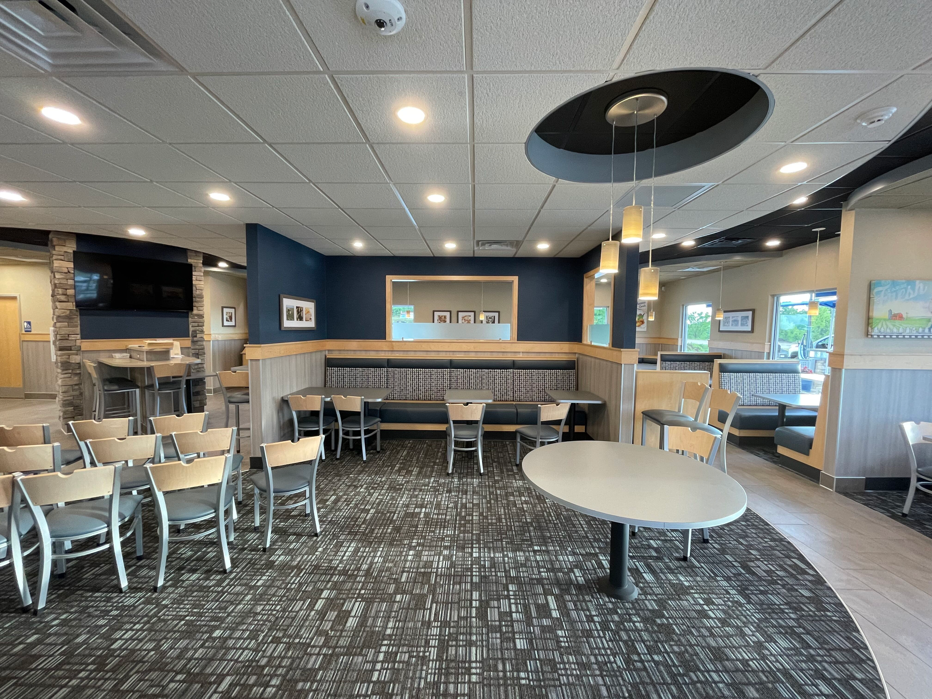 Empty modern café dining area with metal chairs, round tables, and a service counter under recessed lighting