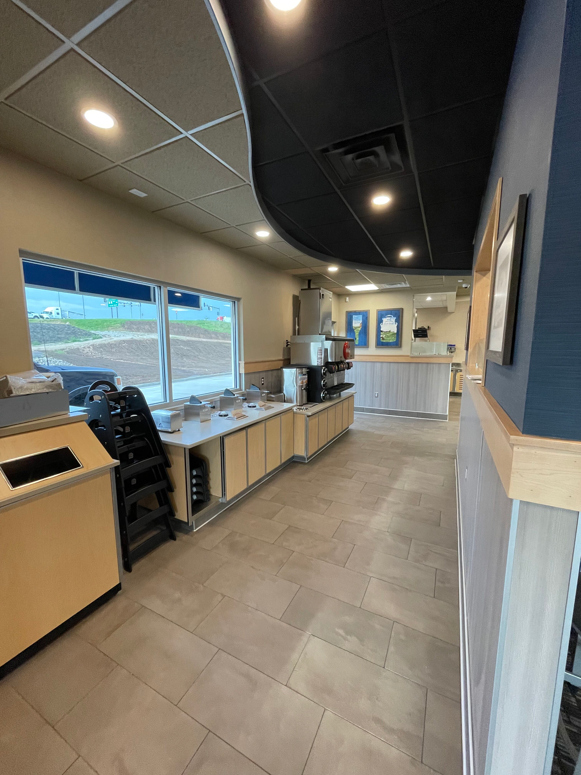 Empty modern cafe counter with beige tile floor, black ceiling accents, and large front windows.