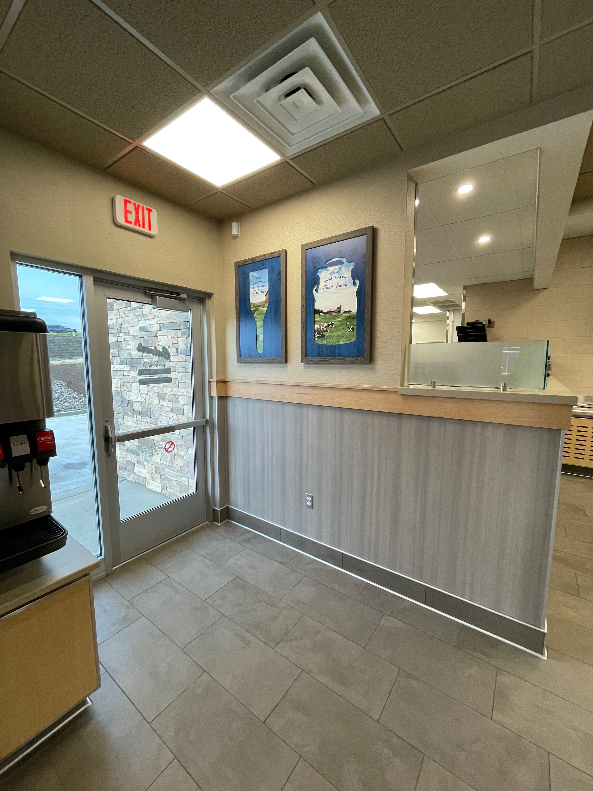 Small lobby with glass entrance, reception counter, tiled floor, framed art, and bright ceiling lights