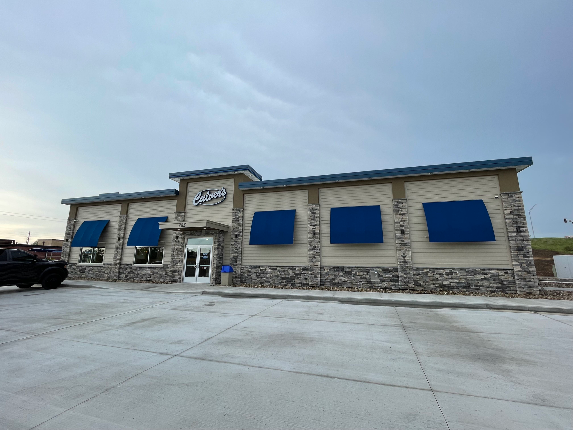 Single-story stone building with blue awnings and a large empty concrete parking lot.