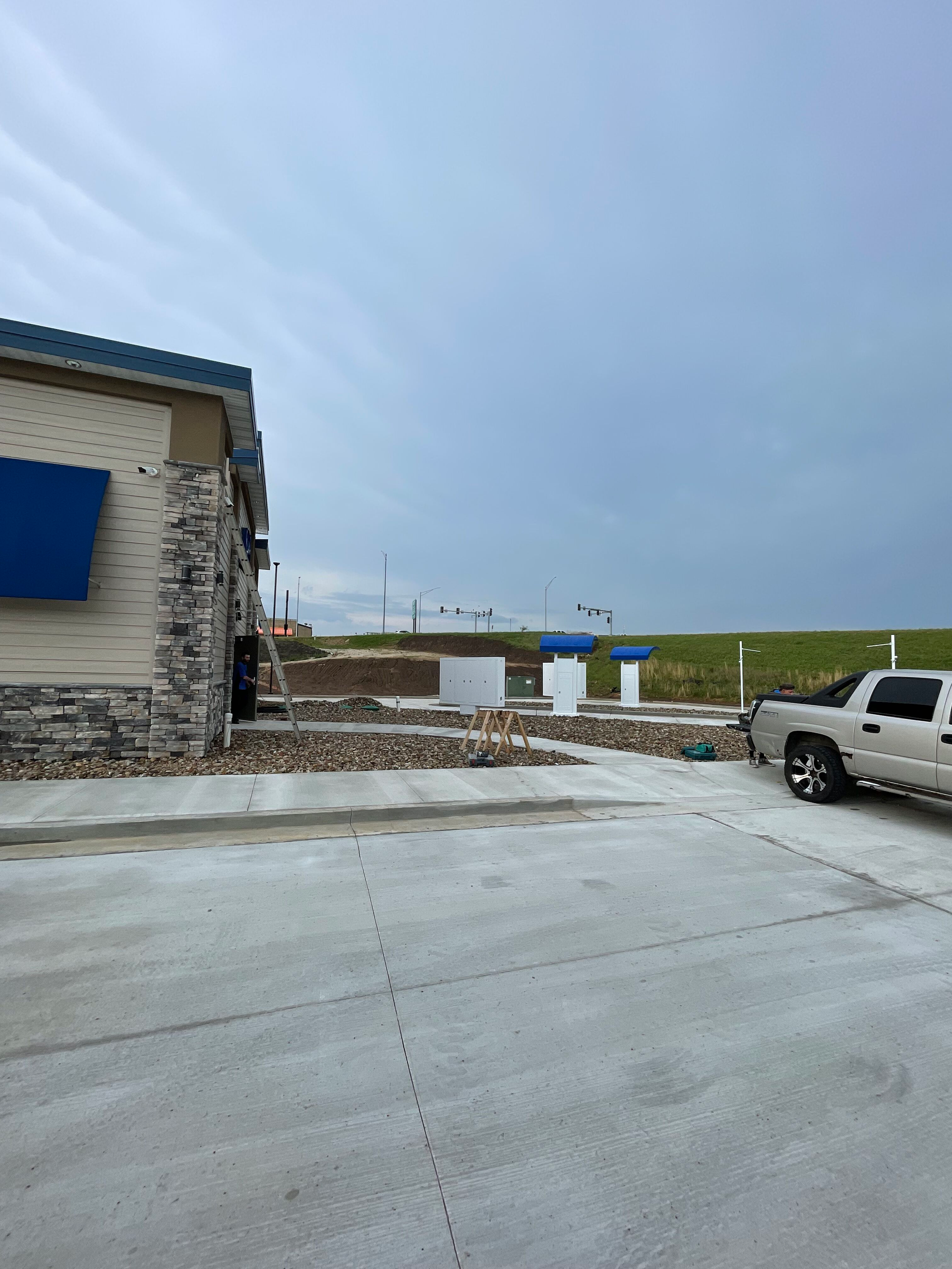 Snowy parking lot beside a stone building with a blue awning and a white pickup truck under a gray sky
