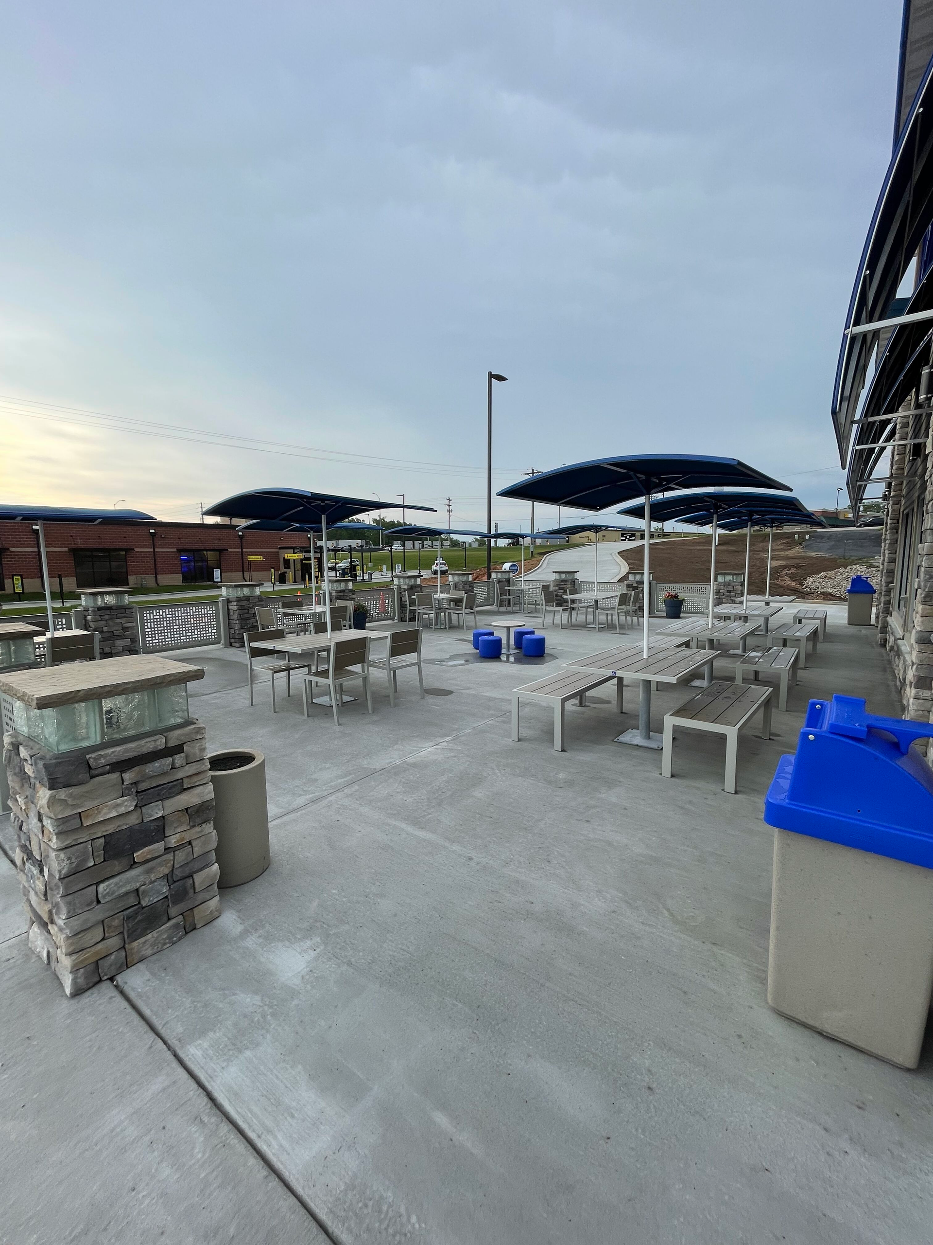 Outdoor patio seating with tables, chairs, and large umbrellas on a concrete terrace at dusk.