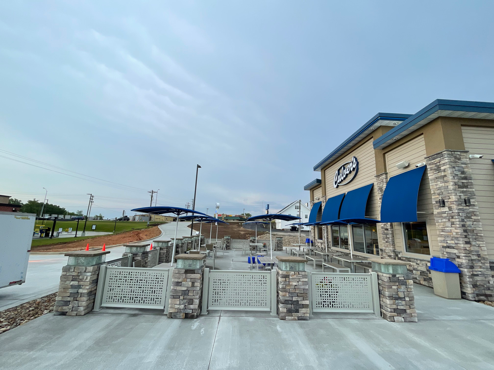 Outdoor restaurant patio with stone walls, blue awnings, and a cloudy sky.