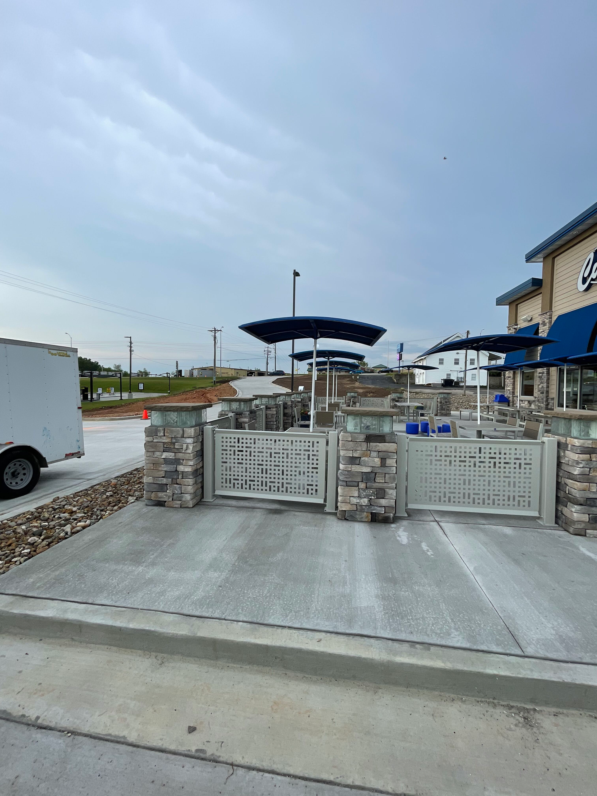 Outdoor patio area with concrete seating, umbrellas, and a building under a cloudy sky