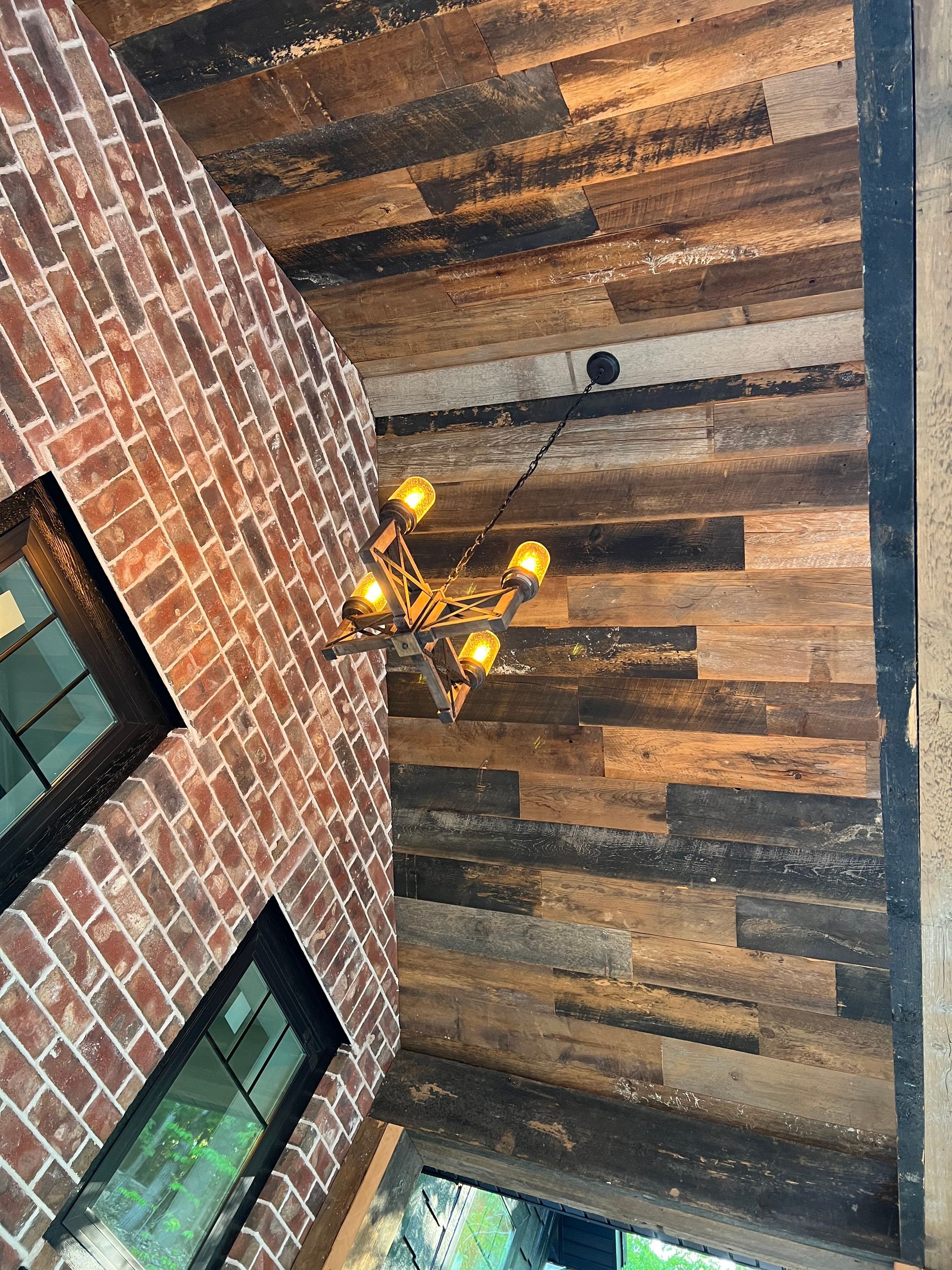 Brick wall and rustic wood ceiling with a hanging chandelier and windows below.
