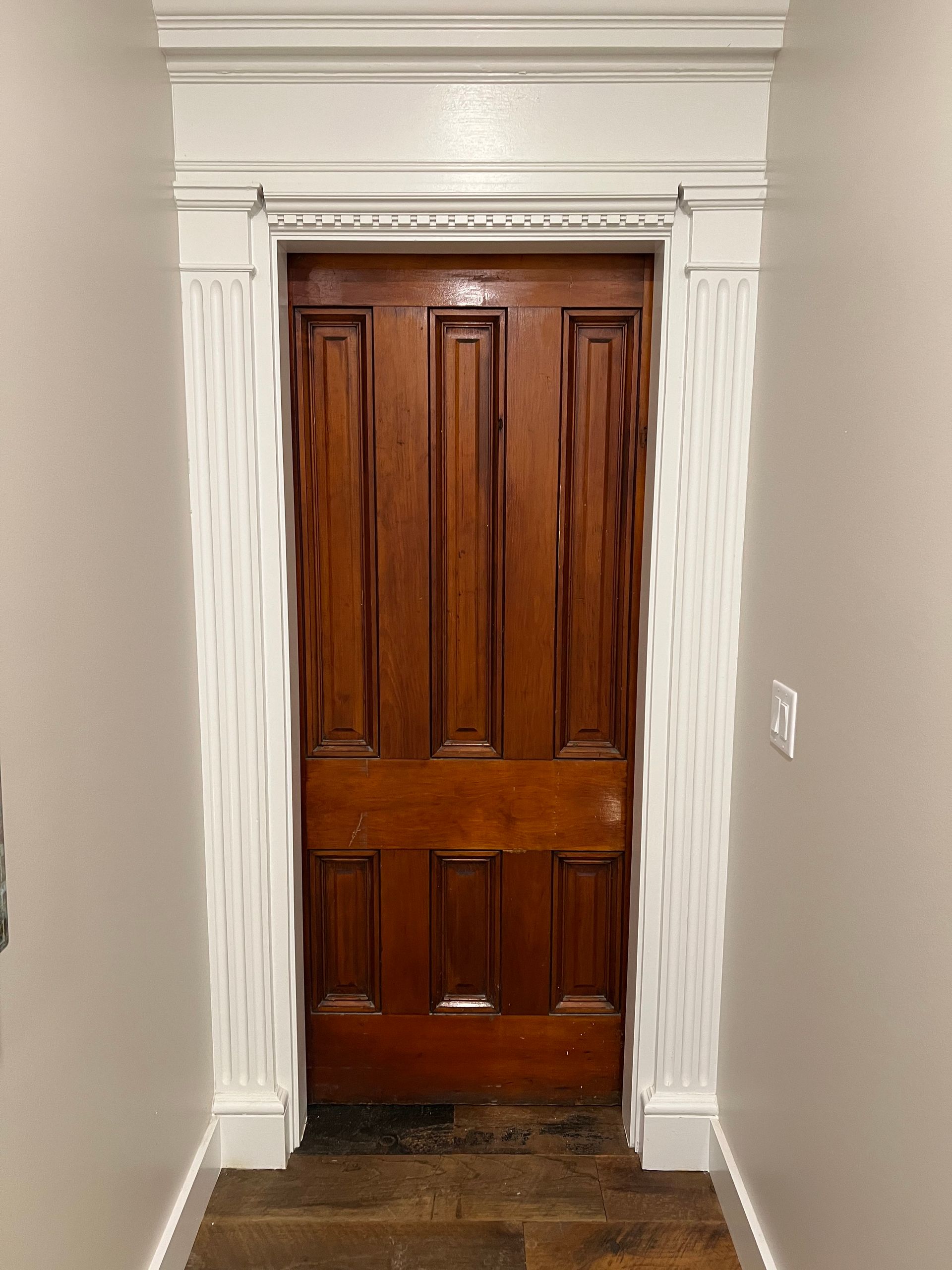 Wooden front door framed by white trim in a narrow hallway