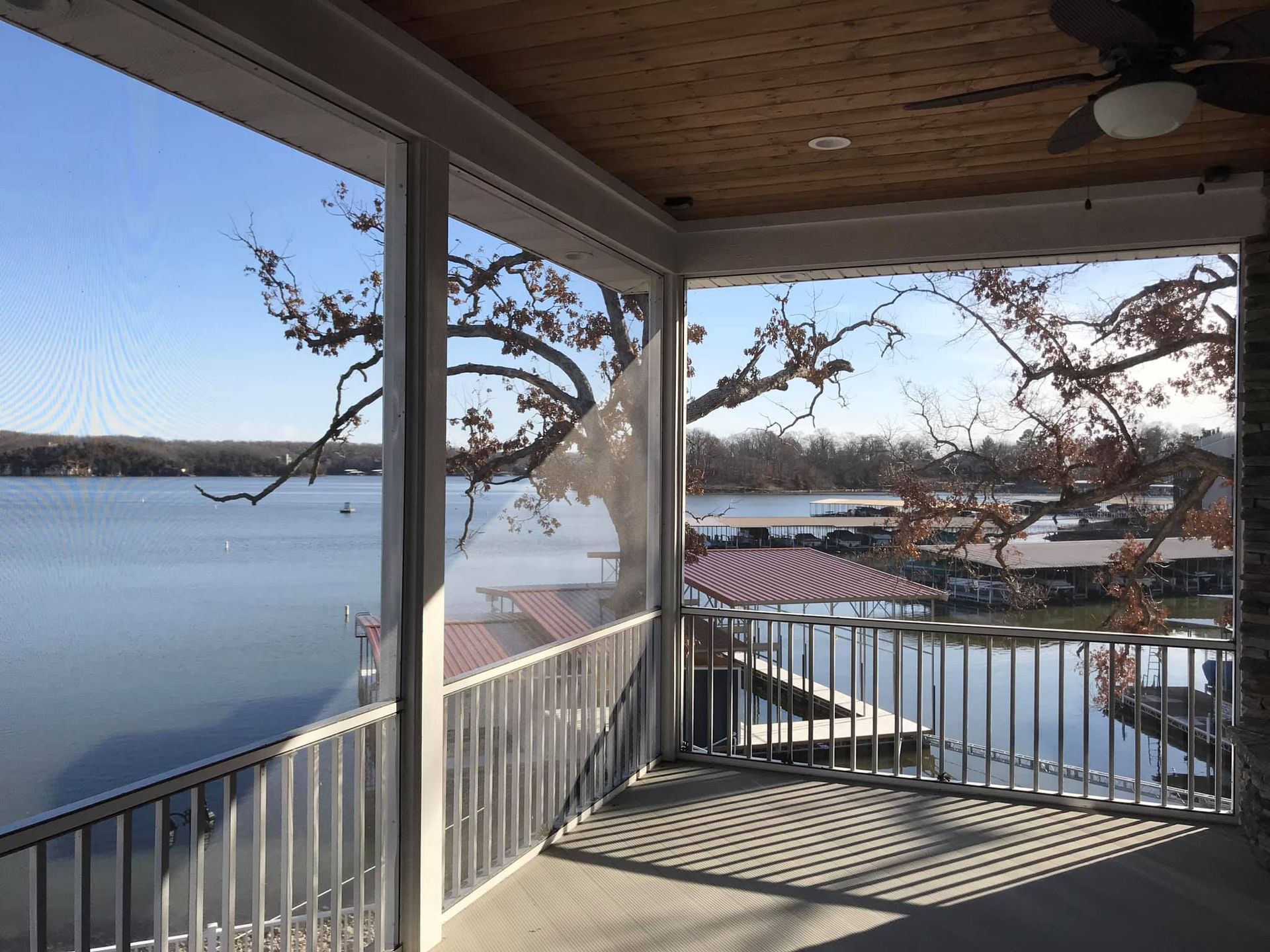 Covered porch overlooking a calm lake at sunset, with white railings and bare tree branches.