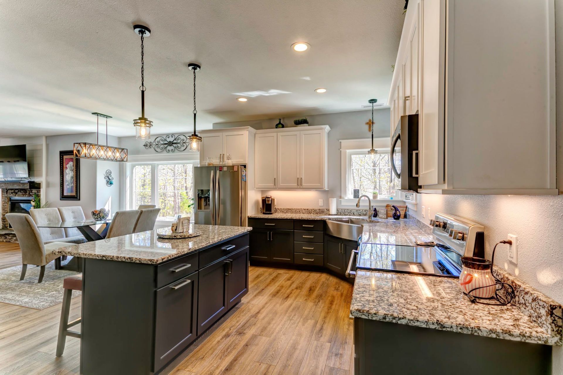 Bright modern kitchen with granite counters, dark island, white cabinets, and hardwood floors adjoining a dining area
