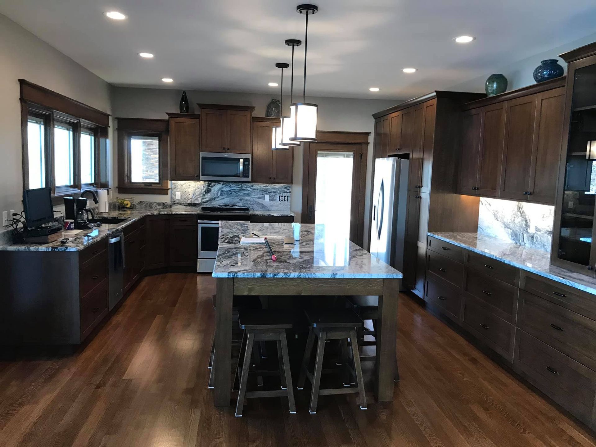 Modern kitchen with dark cabinets, granite island, pendant lights, and hardwood floors