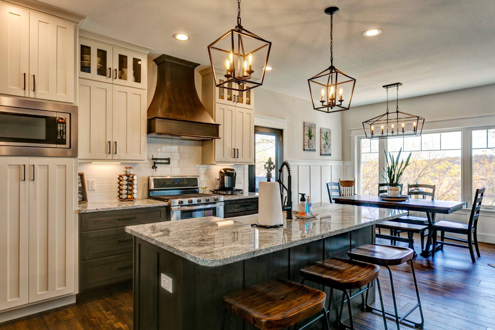 Modern kitchen with granite island, white cabinets, and dining area by large windows