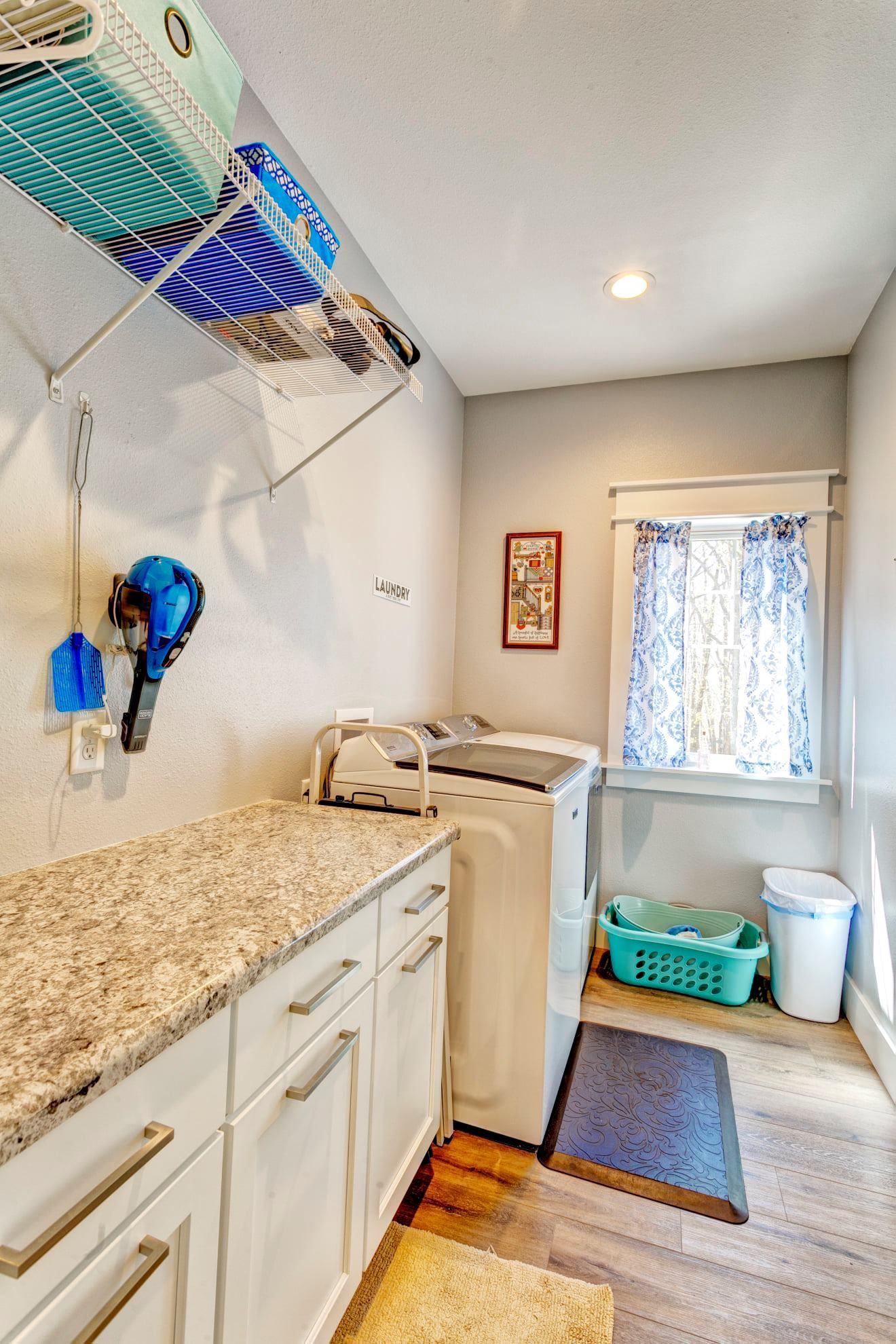 Laundry room with washer and dryer, white cabinets, countertop, and a small window with patterned curtains.
