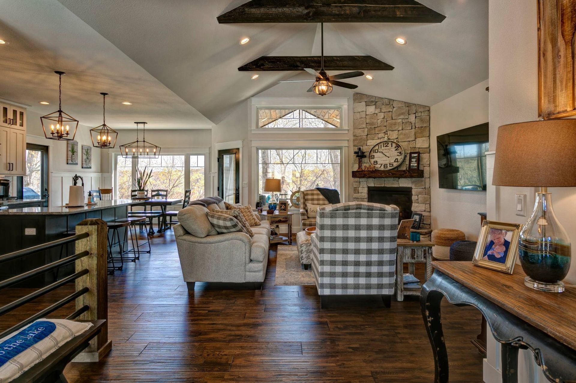 Open-plan living room with gray sofas, dark wood floors, stone fireplace, and kitchen bar seating