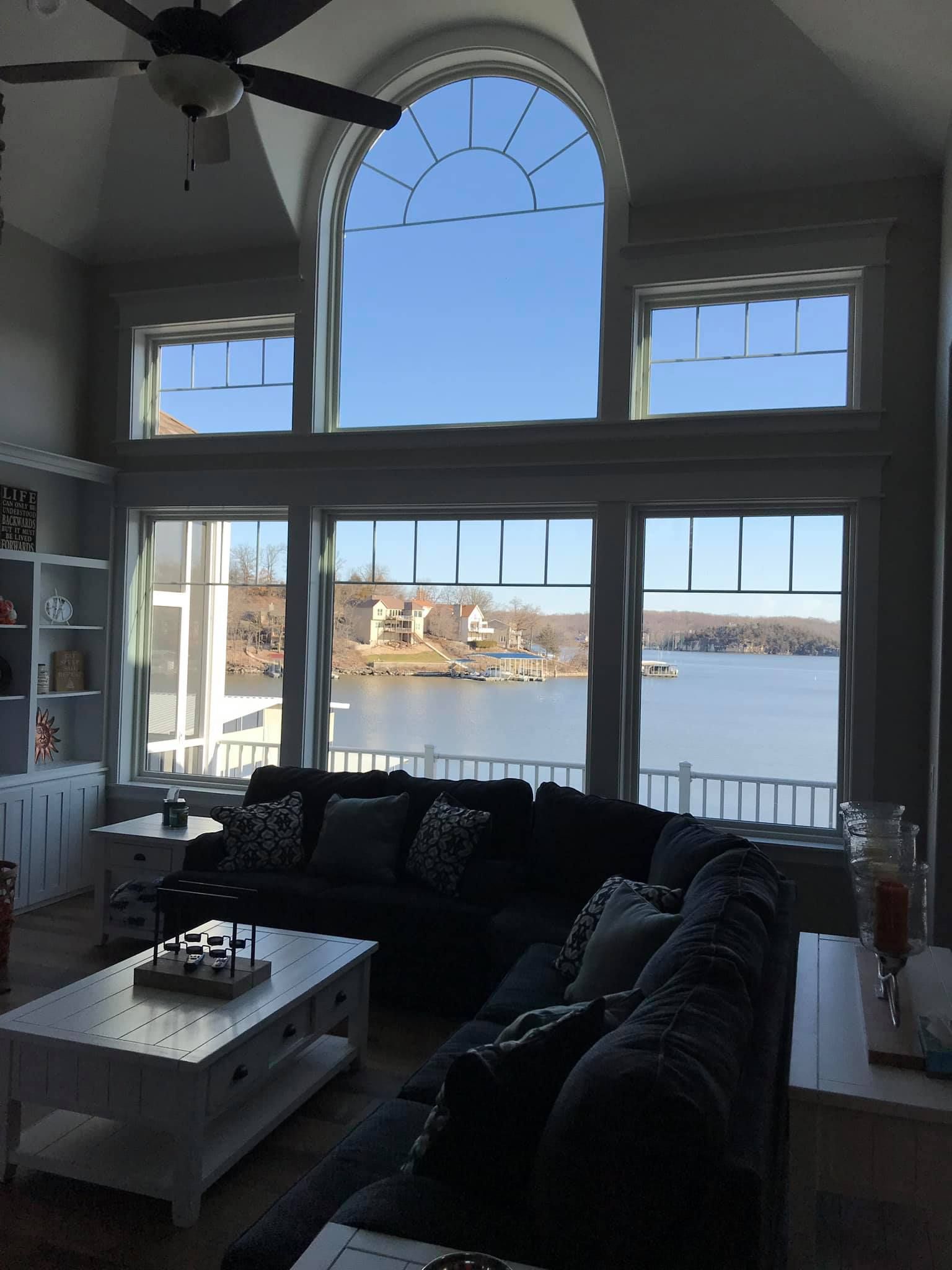 Living room with large arched windows overlooking a calm waterfront and bright blue sky