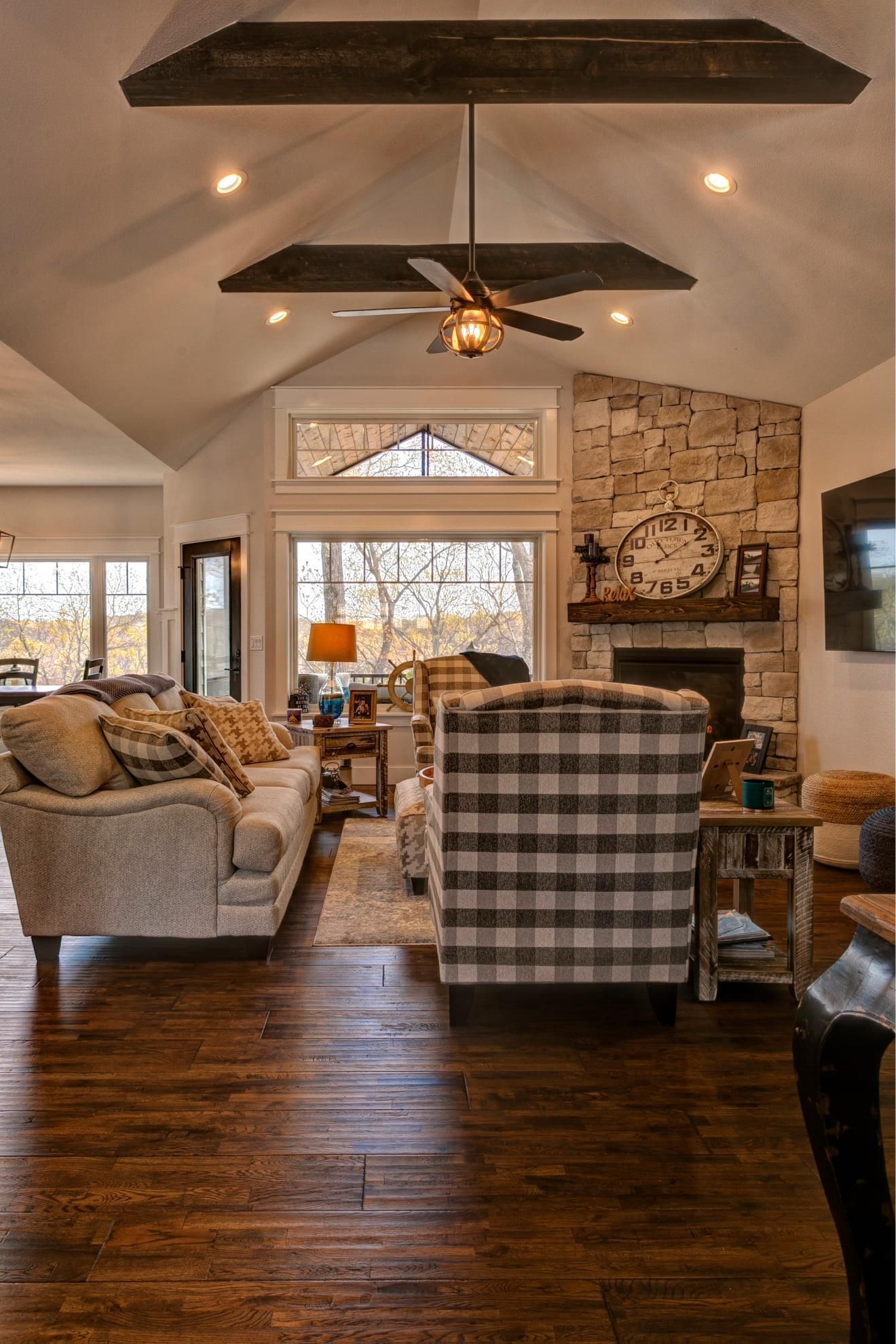 Cozy living room with plaid chairs, fireplace, dark wood floors, and vaulted ceiling with a ceiling fan