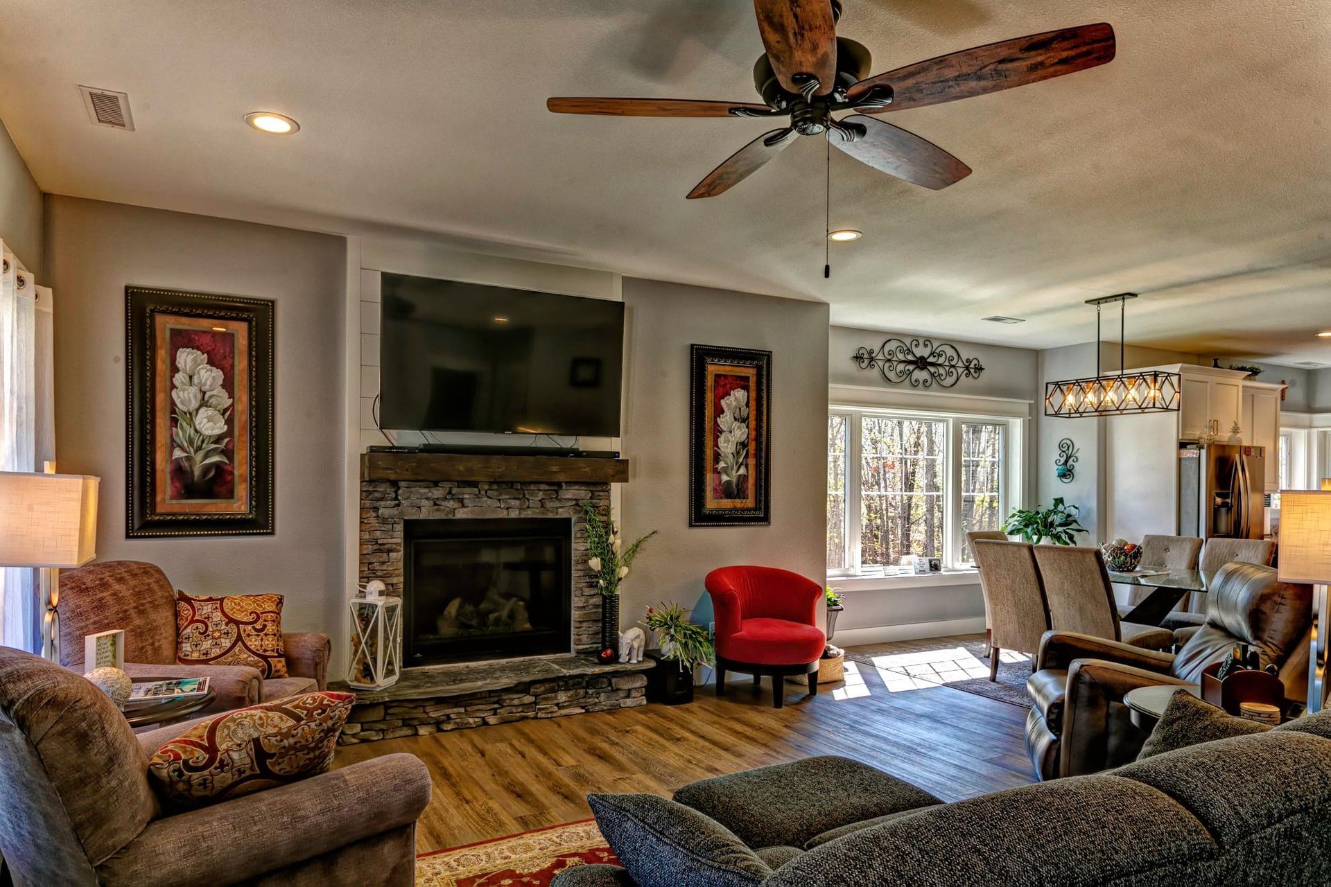 Living room with fireplace, large TV, ceiling fan, and colorful armchairs near a bright window