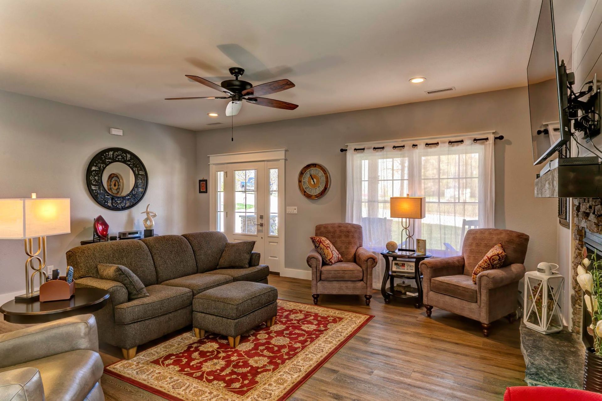 Cozy living room with sectional sofa, two armchairs, lamps, patterned rug, and large windows.