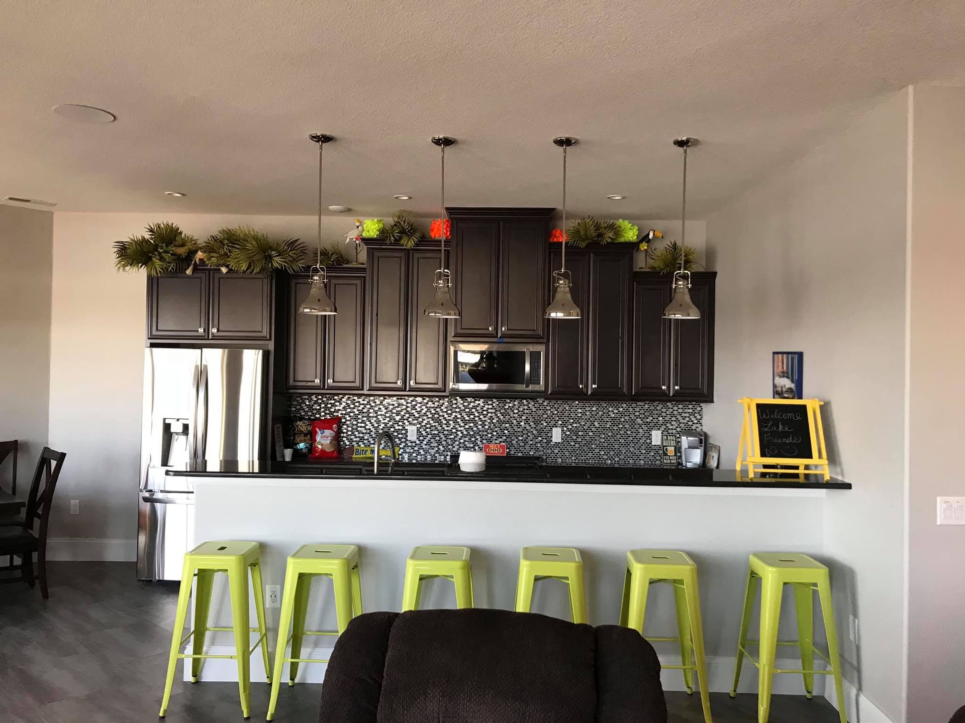 Modern kitchen with dark cabinets, stainless fridge, white island, and lime green bar stools