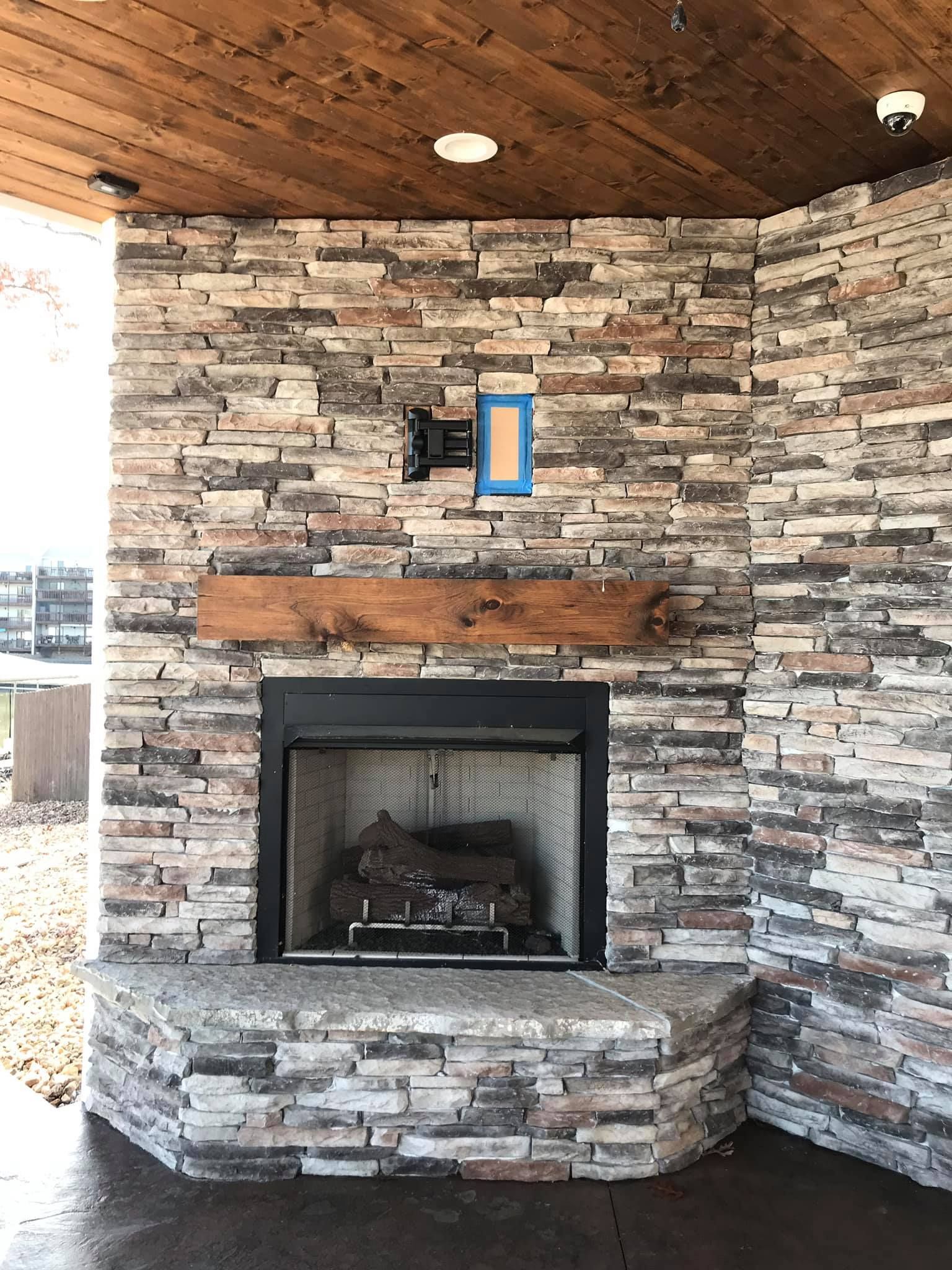 Stone fireplace on a covered porch with a wooden ceiling and a small blue-framed window above the mantel