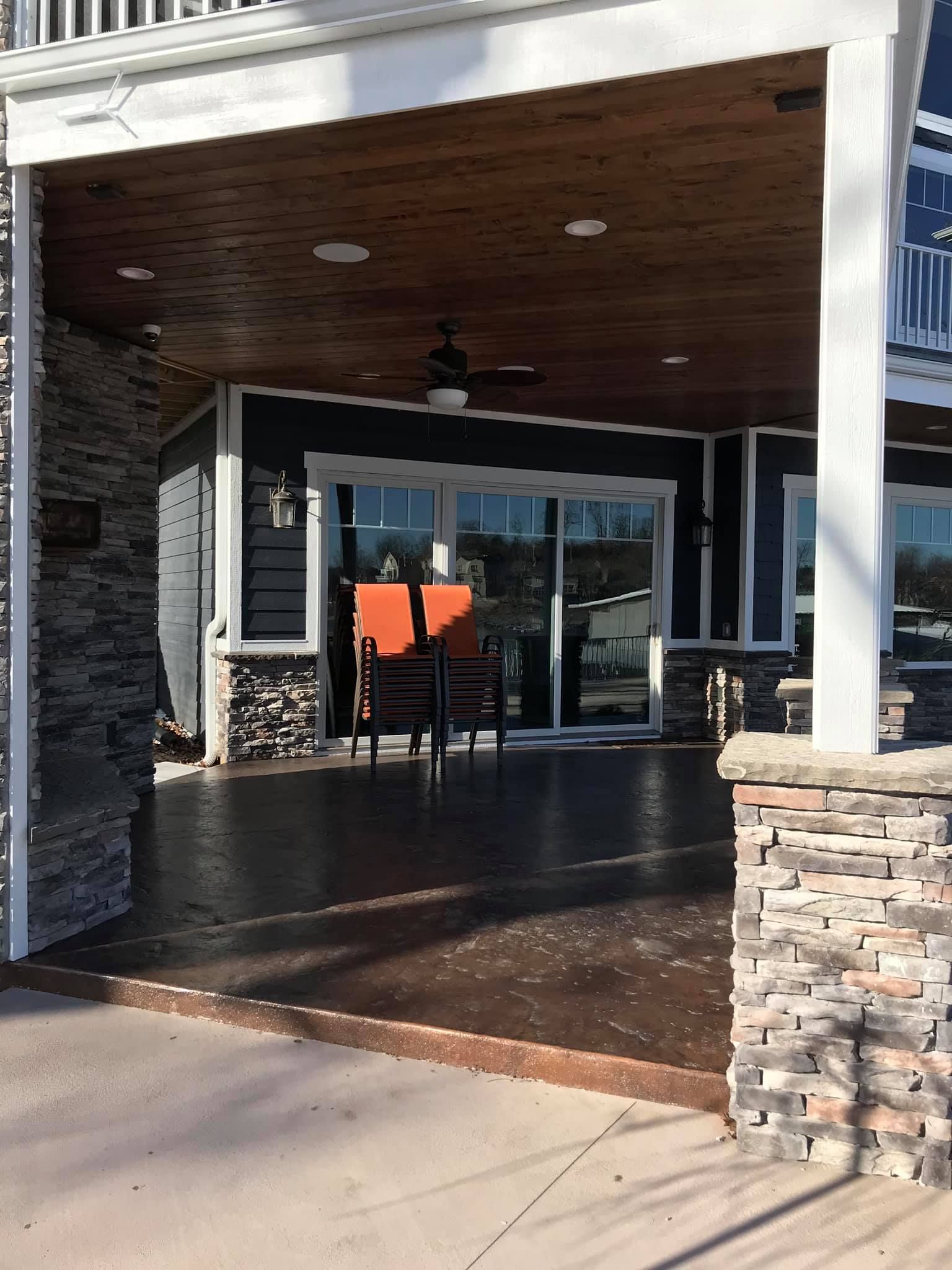 Covered patio entrance with glass doors, black chairs, orange cushions, and stone columns.
