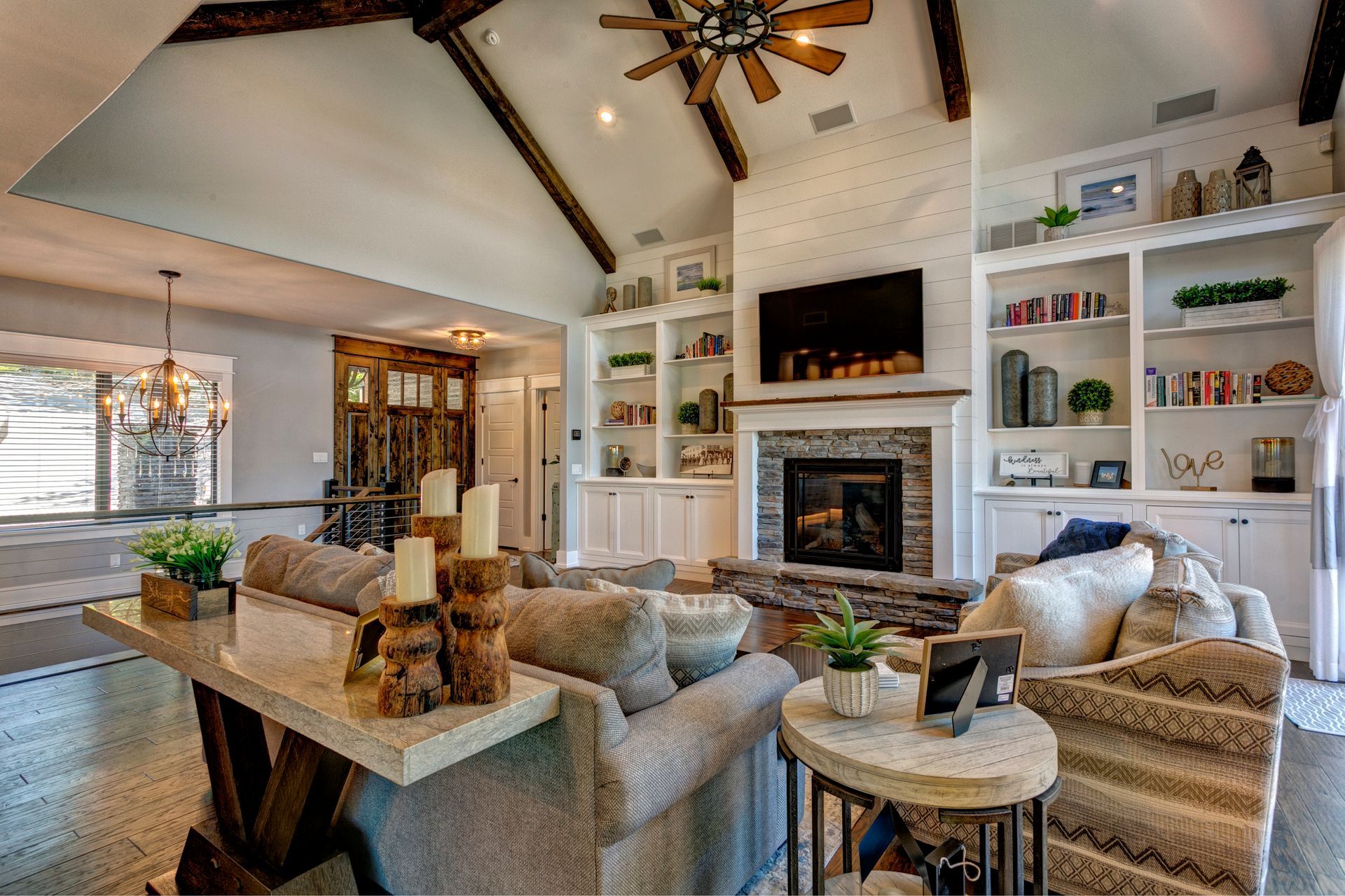 Bright living room with vaulted ceiling, fireplace, TV, built-in shelves, and beige upholstered seating